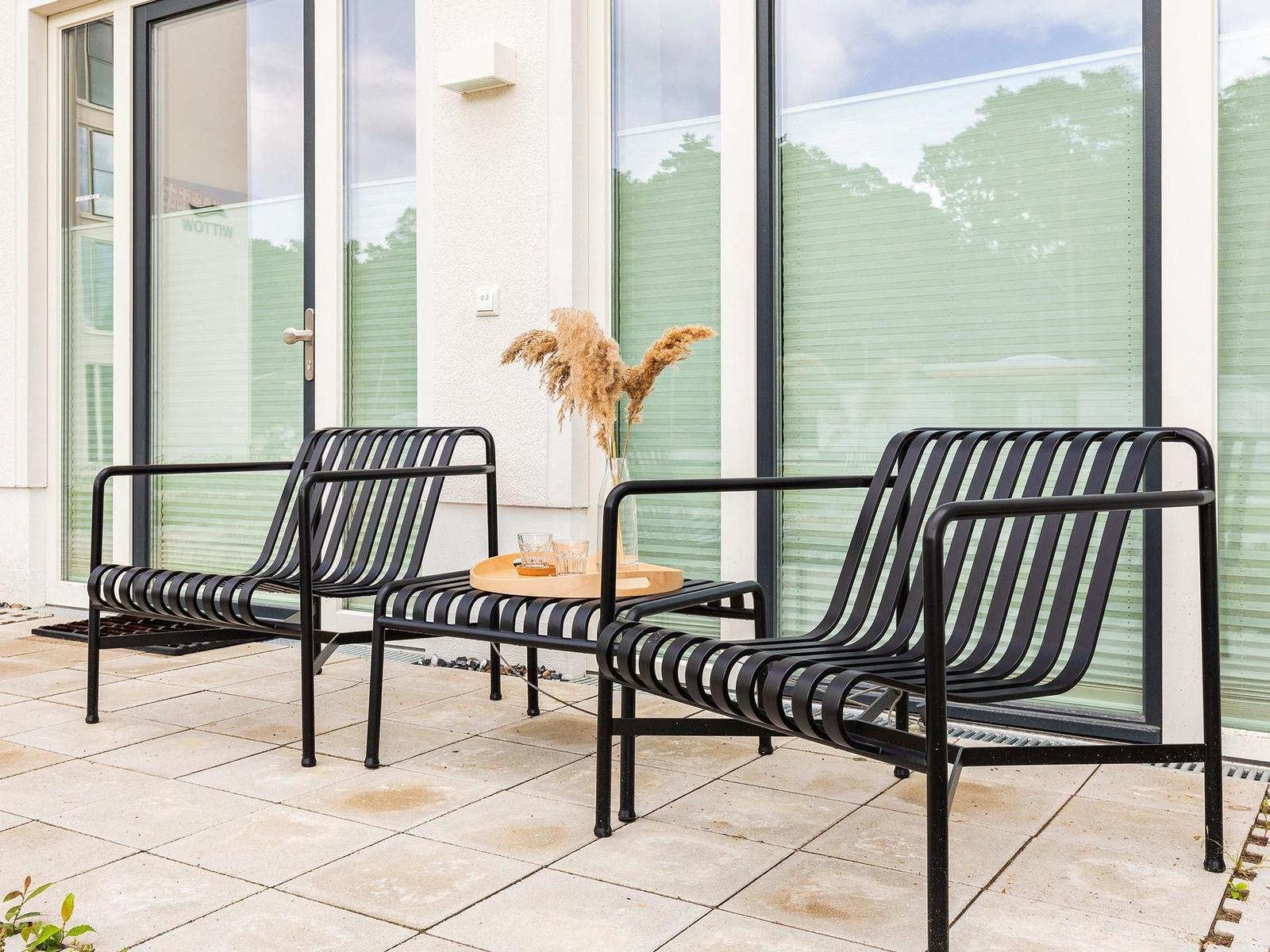 Terrasse mit zwei schwarzen Metallstühlen und einem runden Holztisch.