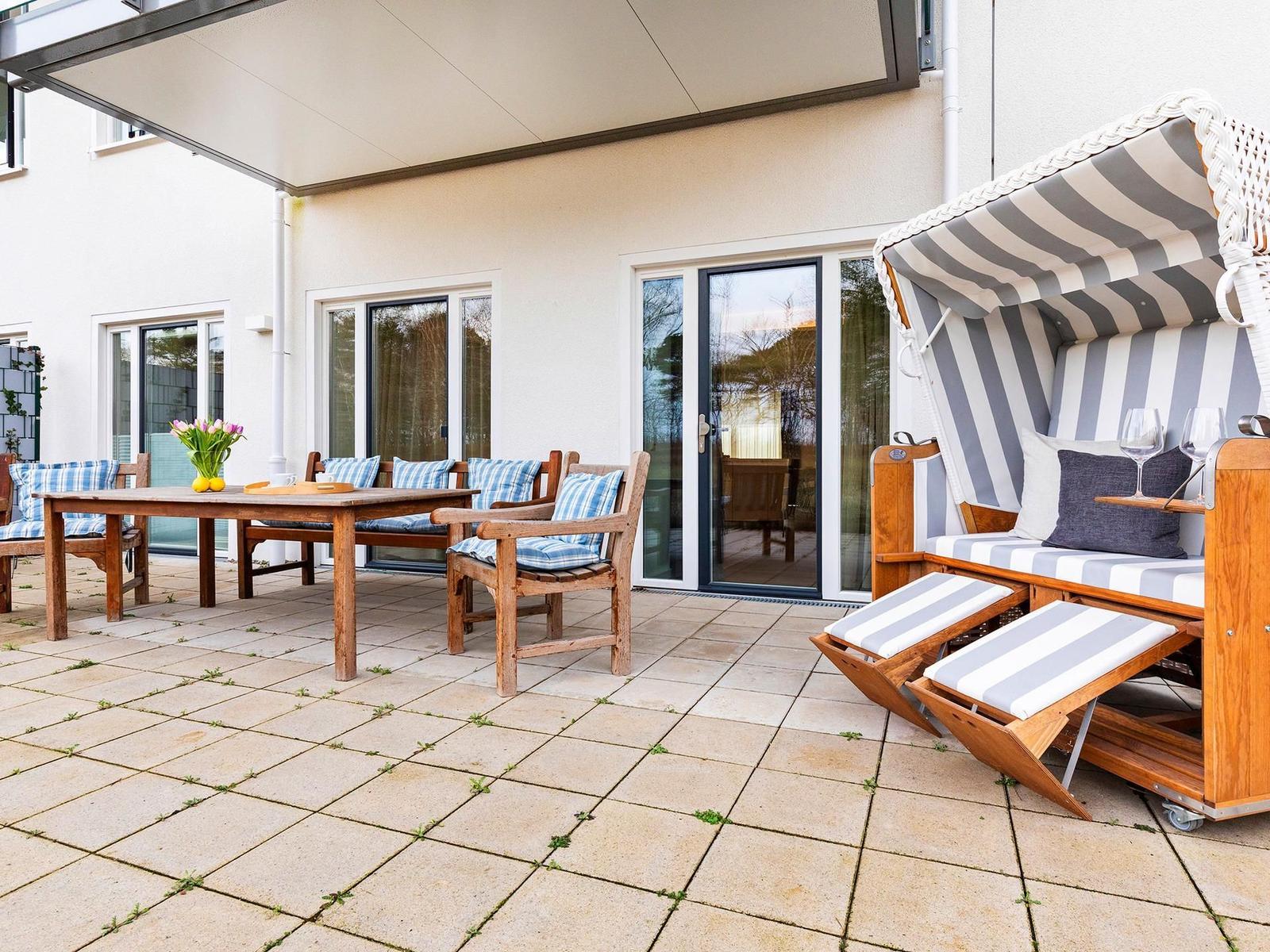 Terrasse mit Holztisch, Stühlen und Strandkorb mit Streifenbezug.