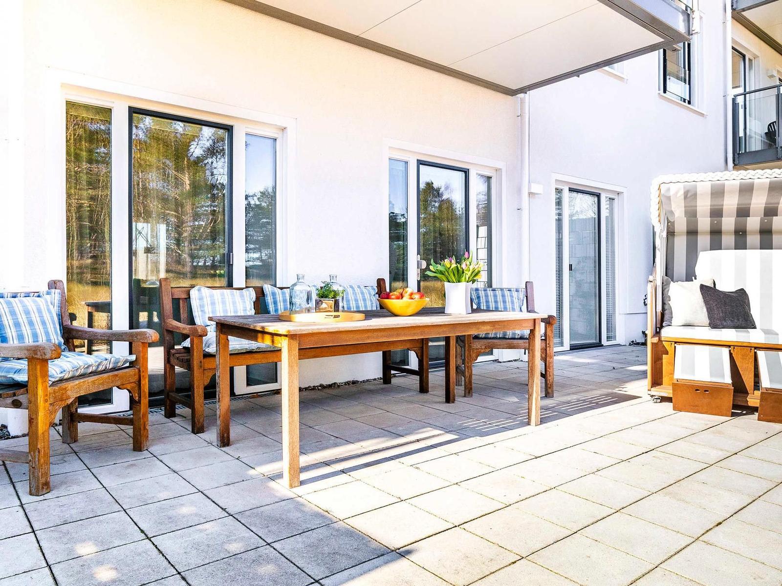 Terrasse mit Holztisch, Stühlen und Sonnenschutz. Hintergrund: Haus mit Fenstern.