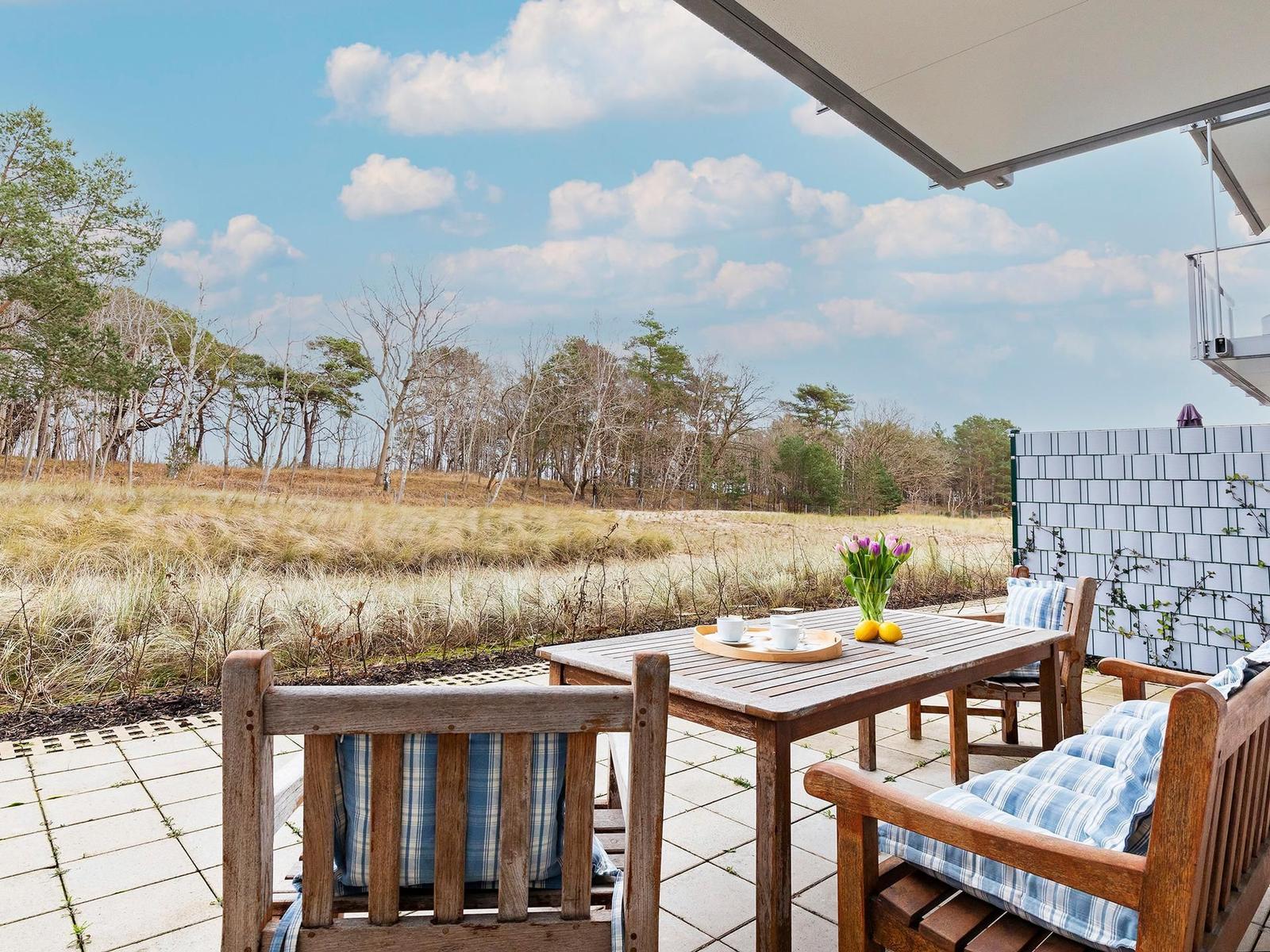 Terrasse mit Holztisch und Bänken, Blick auf Wald und Himmel.