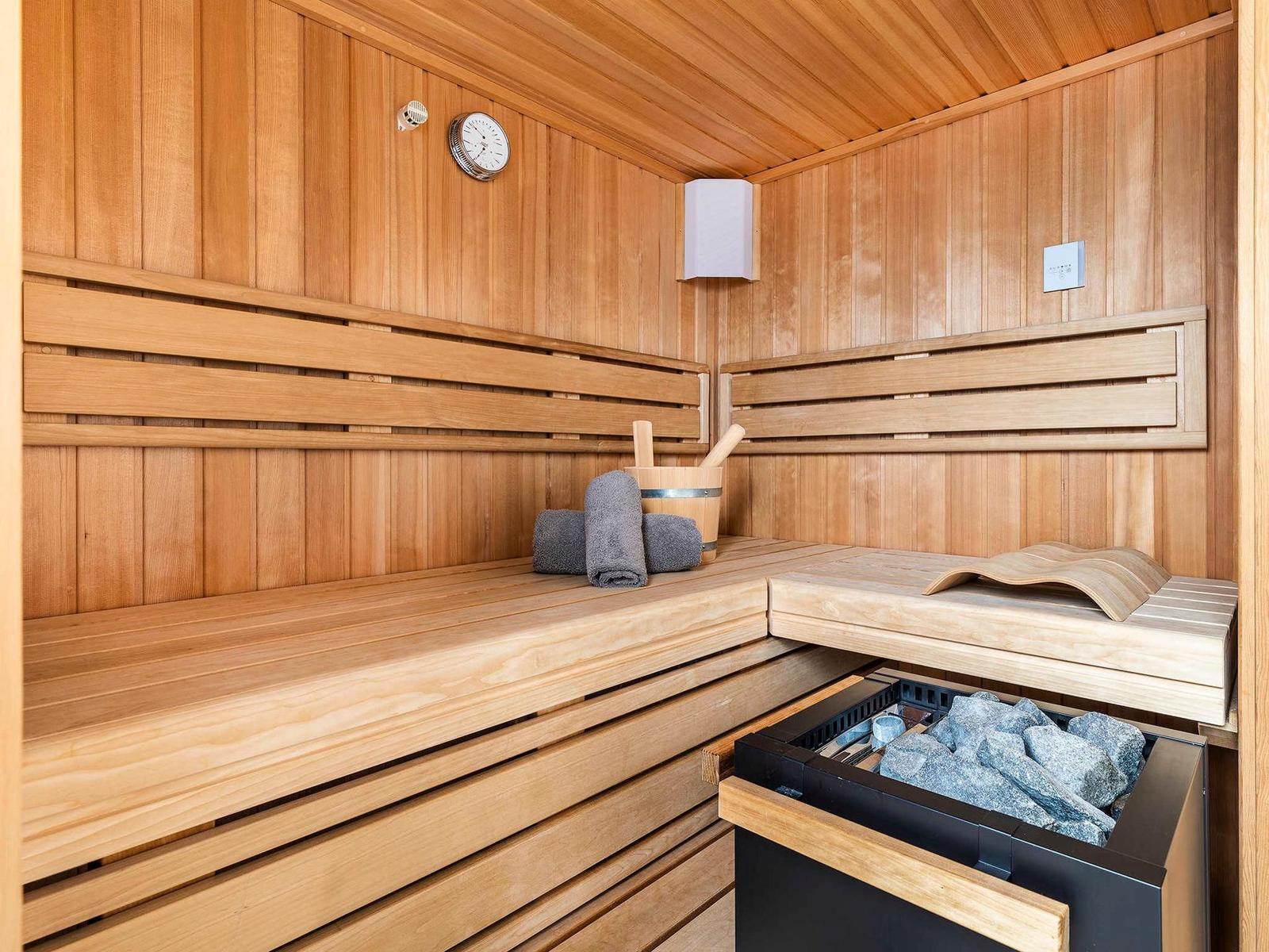 Sauna mit Holzbank, Thermometer und Steinen im Ofen.