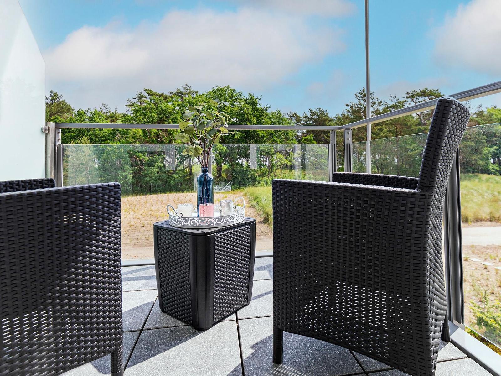 Terrace with two black wicker chairs and table. Glass railing and forest in background.