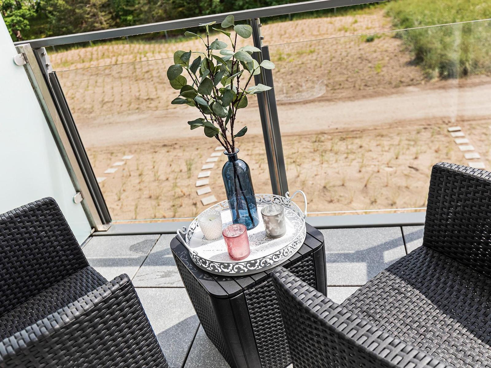 Terrace with two chairs and a table. On it is a vase with plant and candles.