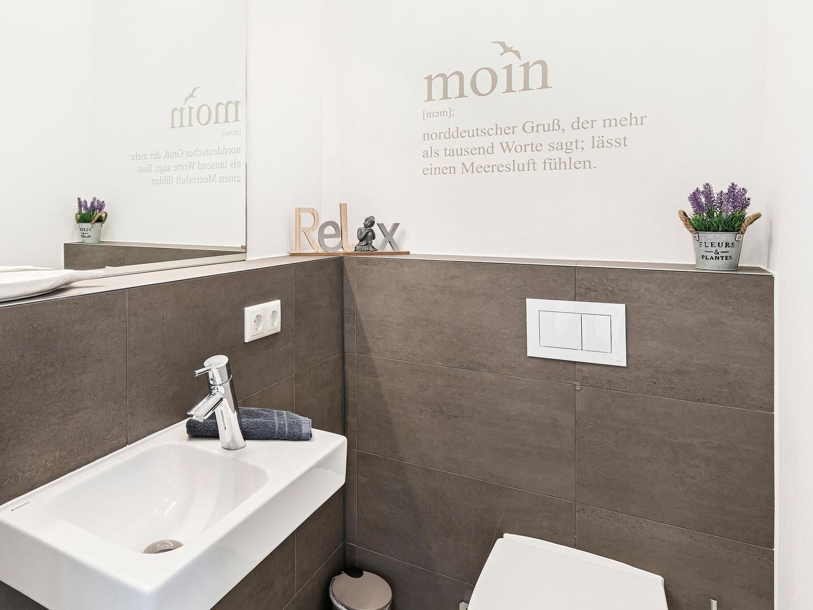 Bathroom with sink, mirror, and toilet. Wall decoration with text and plants.