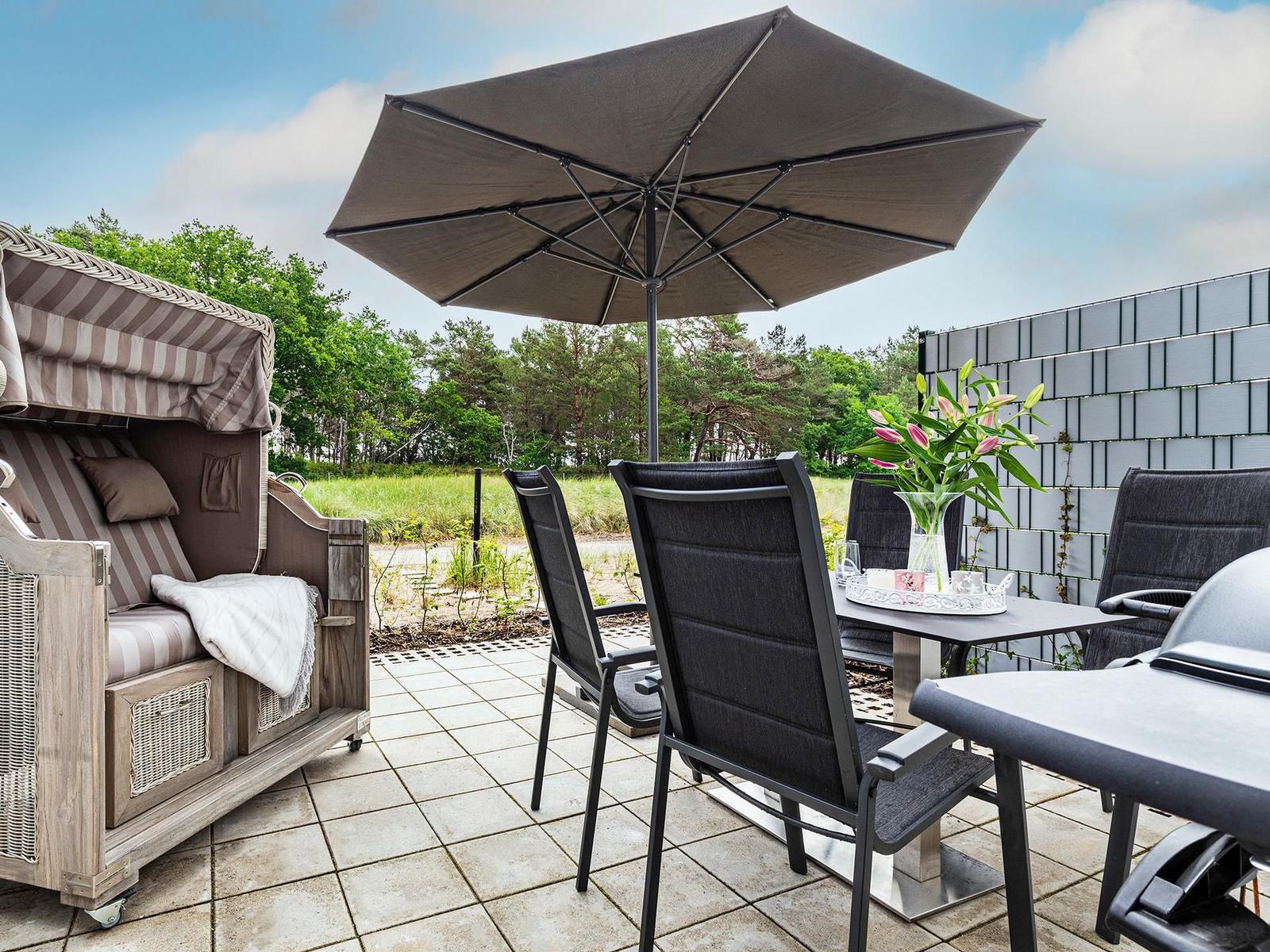 Terrace with umbrella, lounge chair, and dining table with flowers.