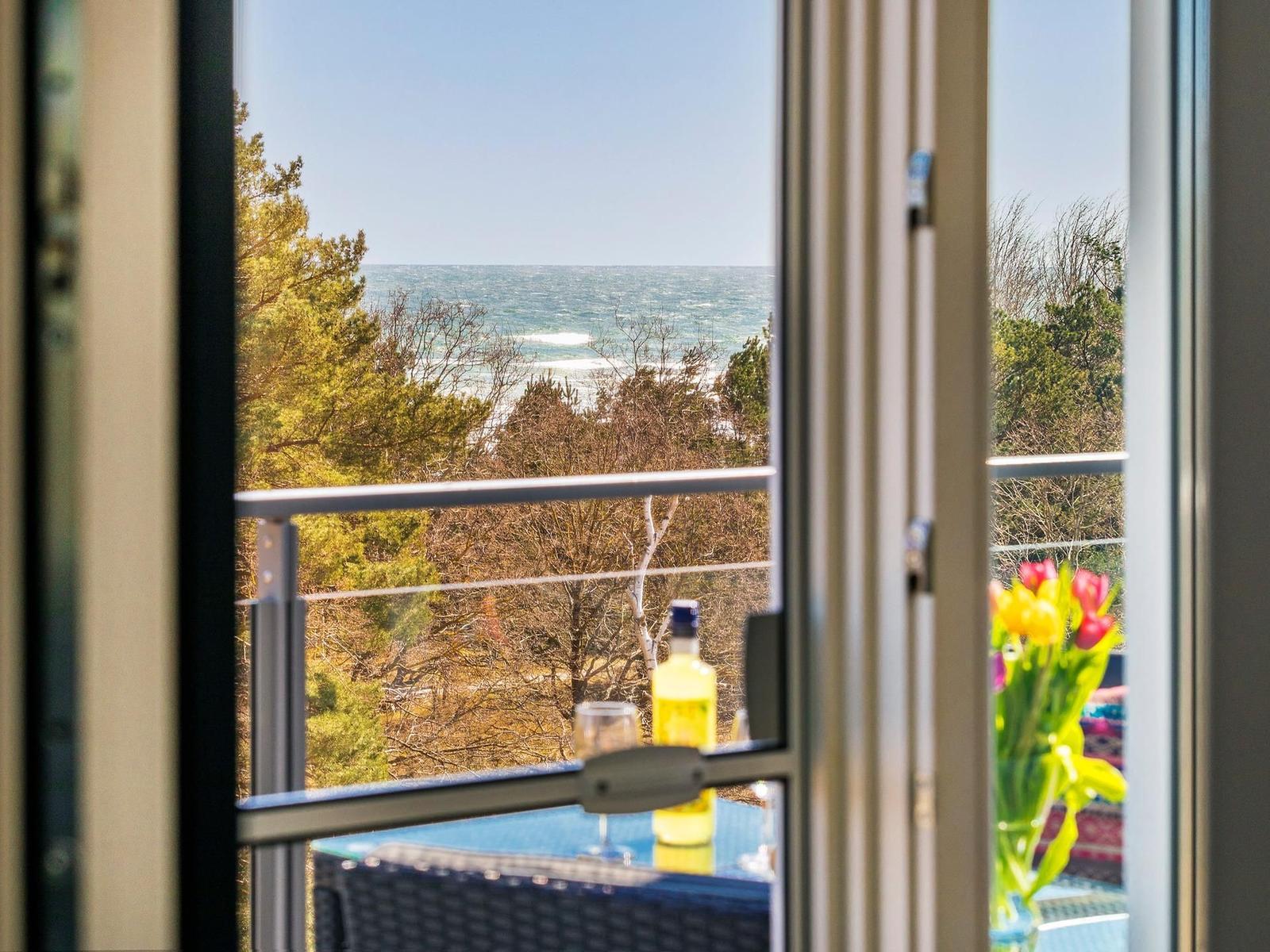 Blick vom Balkon auf das Meer mit Bäumen im Vordergrund und einer Flasche auf dem Tisch.