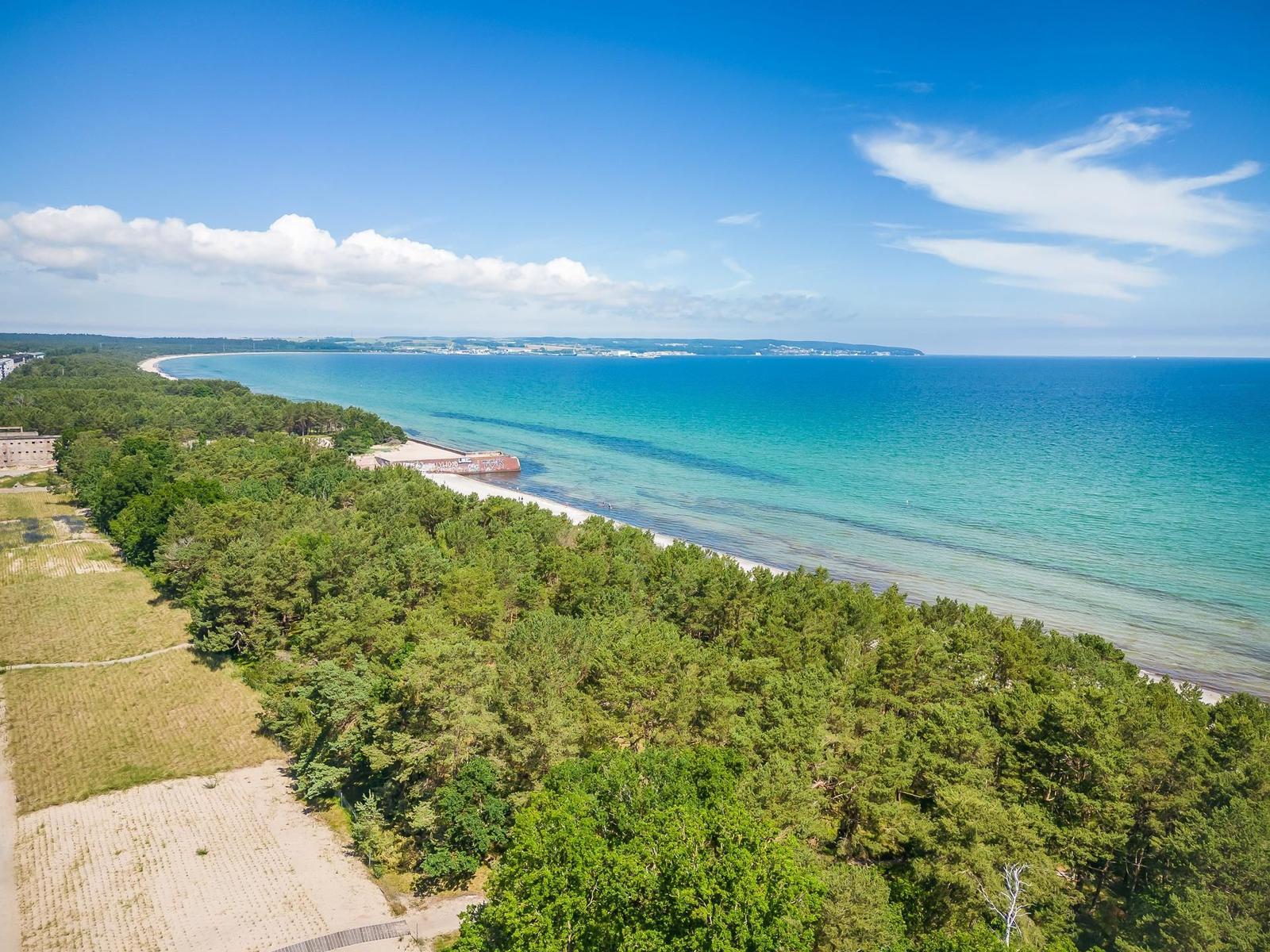 Strand mit klarem Wasser, grüner Landschaft und blauem Himmel.