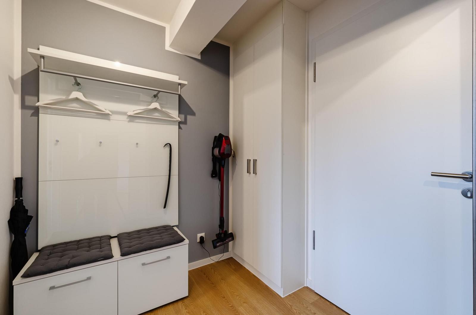 Eingangsbereich mit Garderobe, Sitzbank und Staubsauger. Holzboden und weiße Schränke.