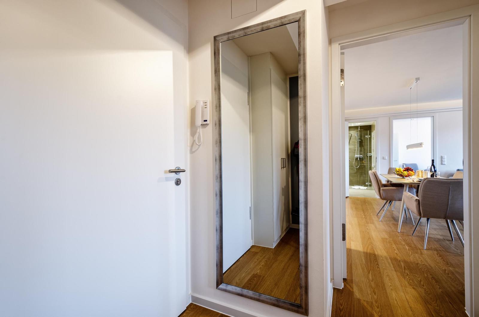 Eingangsbereich mit Spiegel, Tür und Blick in Esszimmer mit Tisch und Stühlen.