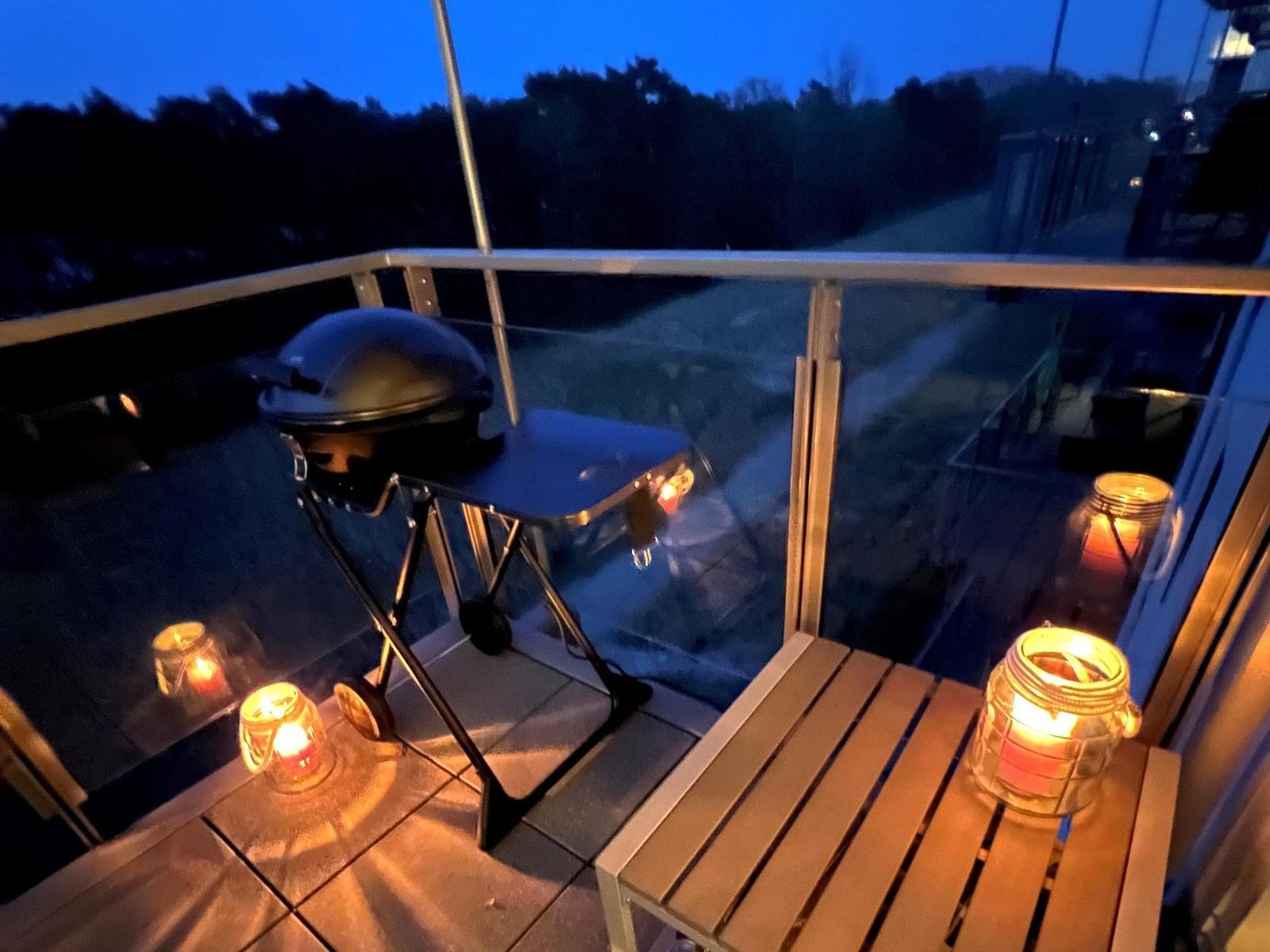 Terrasse mit Grill, Holztisch und Kerzen bei Dämmerung.