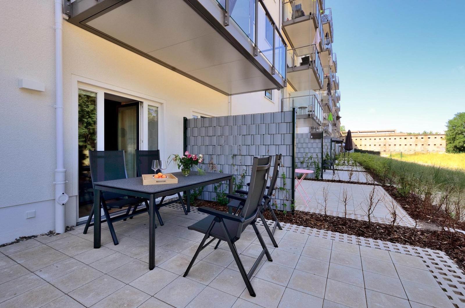 Terrasse mit Tisch, Stühlen und Blumen. Hinterhof mit Pflanzen und Steinplatten.
