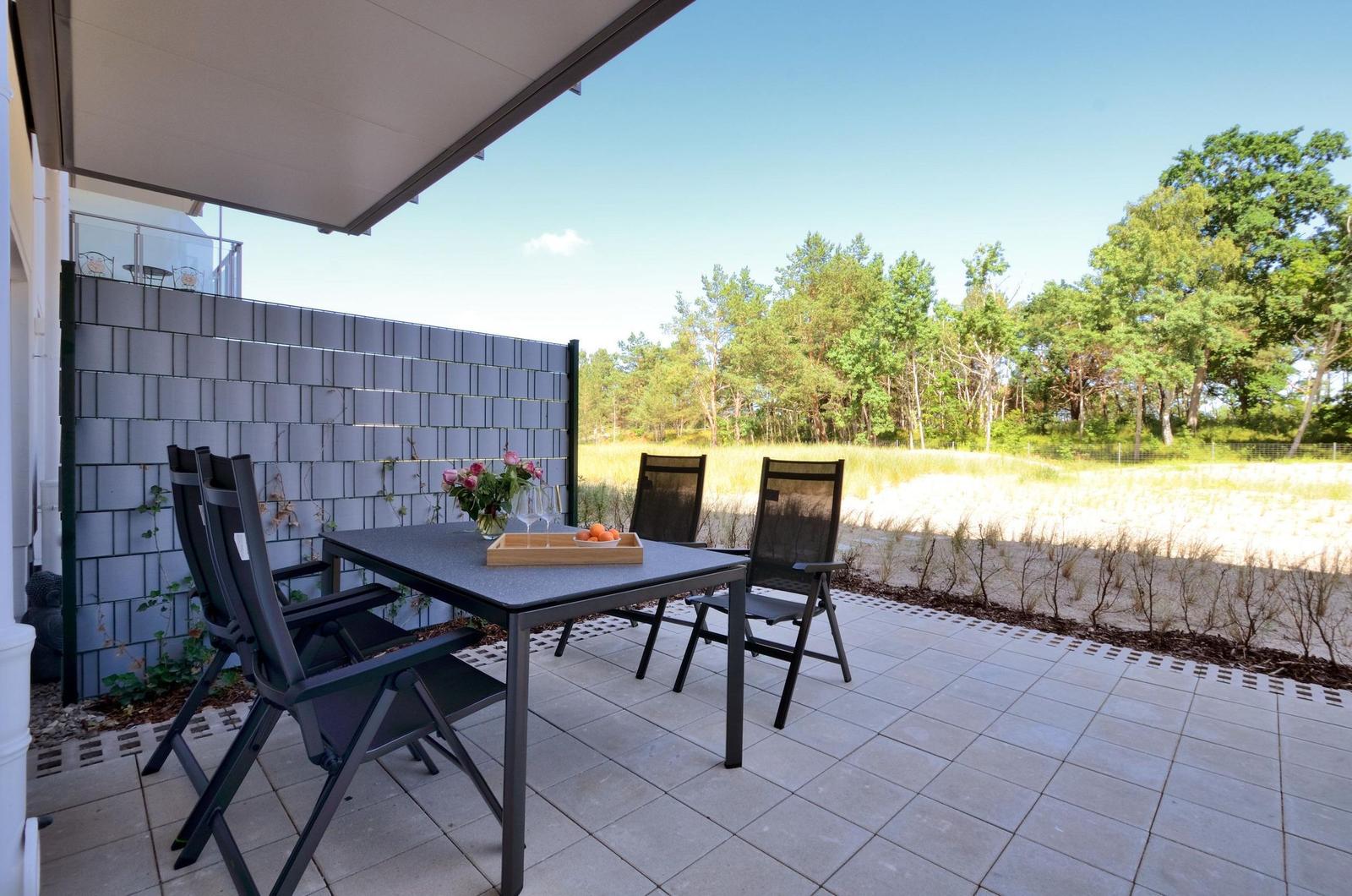 Terrasse mit Tisch und Stühlen, Blick auf Wald und Sandstrand.
