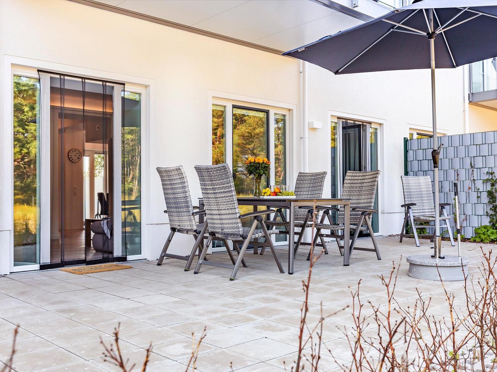 Terrasse mit Tisch, Stühlen und Sonnenschirm. Durchgehende Glasschiebetüren zum Innenraum.