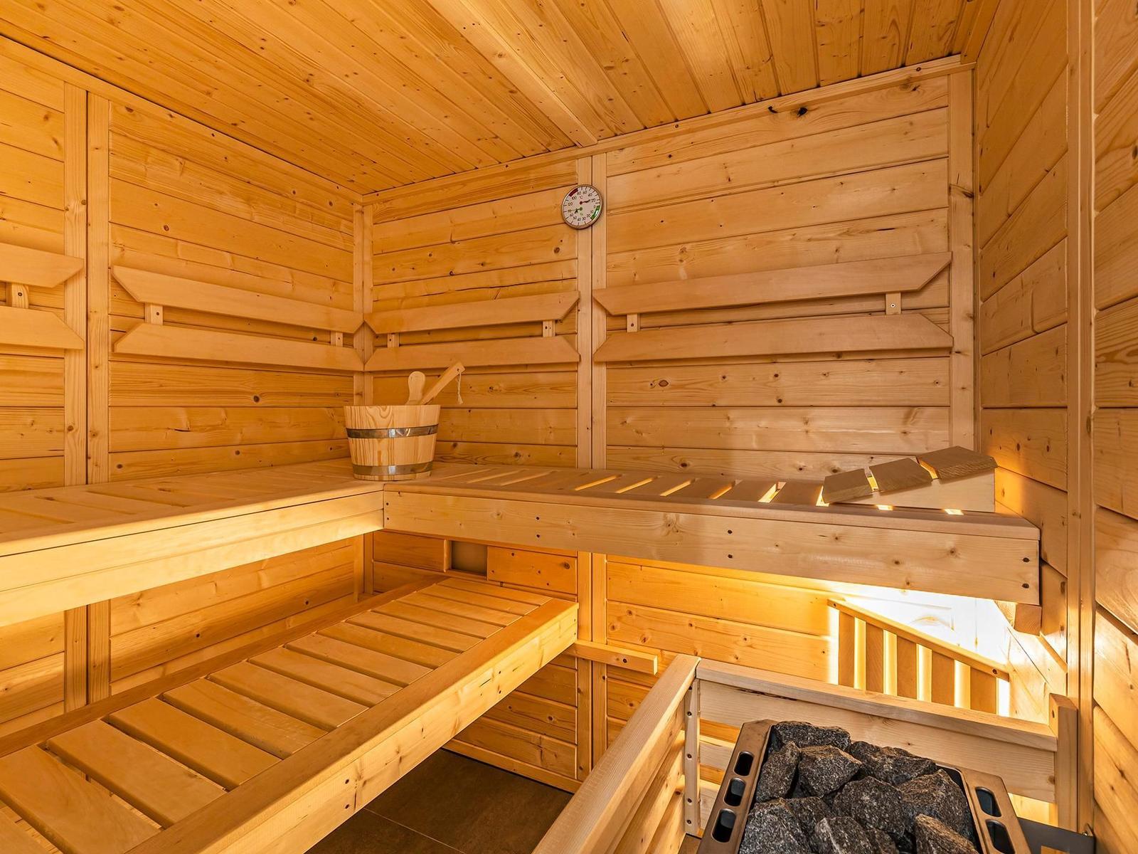 Holzsauna mit Sitzbänken, Körbchen und Temperaturuhr.