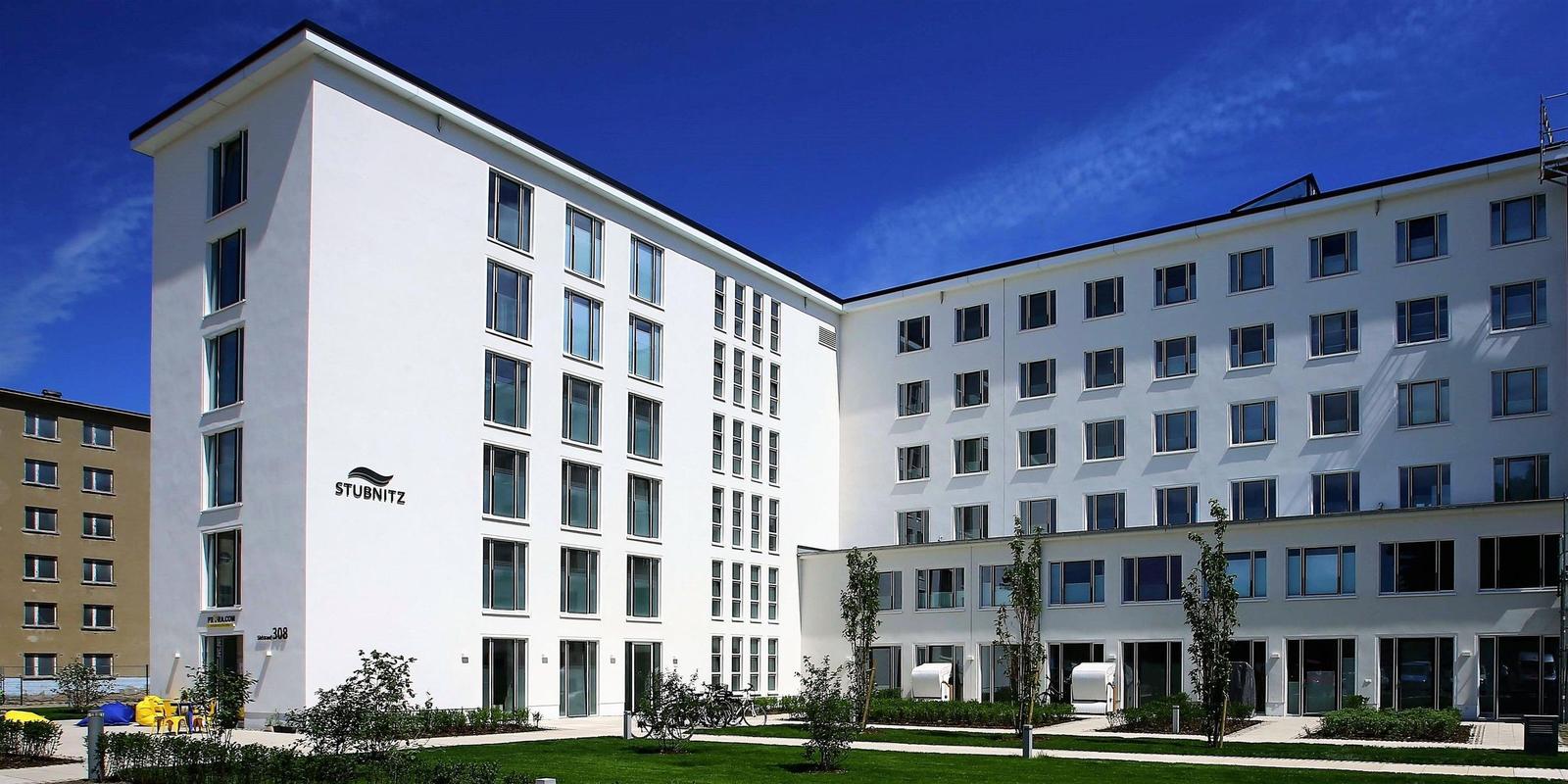 Modernes weißes Gebäude mit vielen Fenstern und grünem Außenbereich.