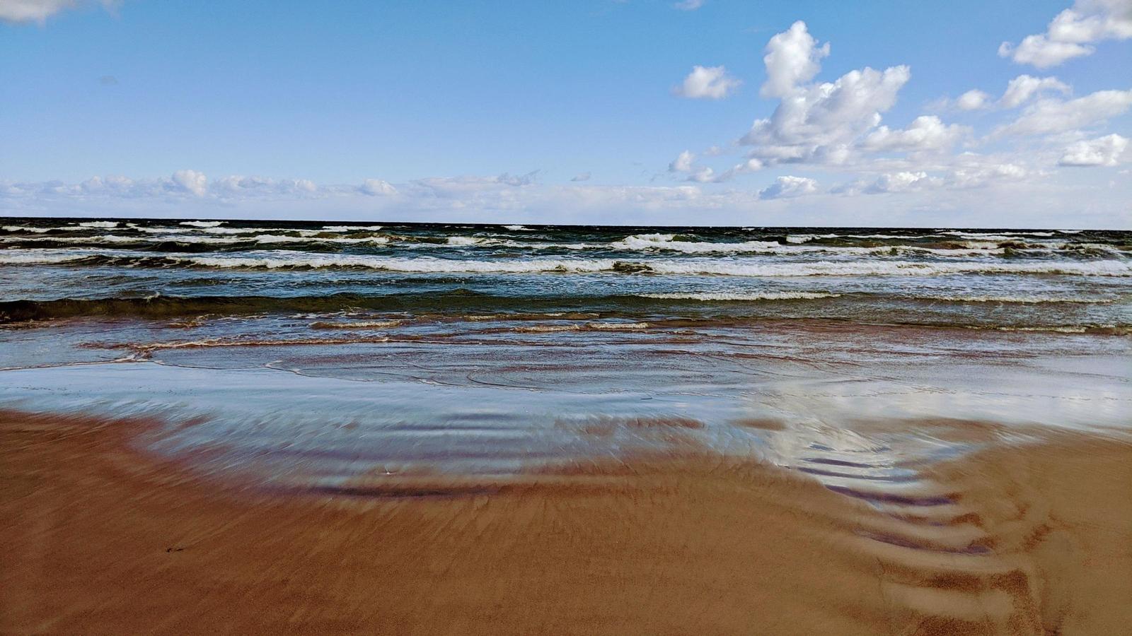 Strand mit Wellen und blauem Himmel mit weißen Wolken.