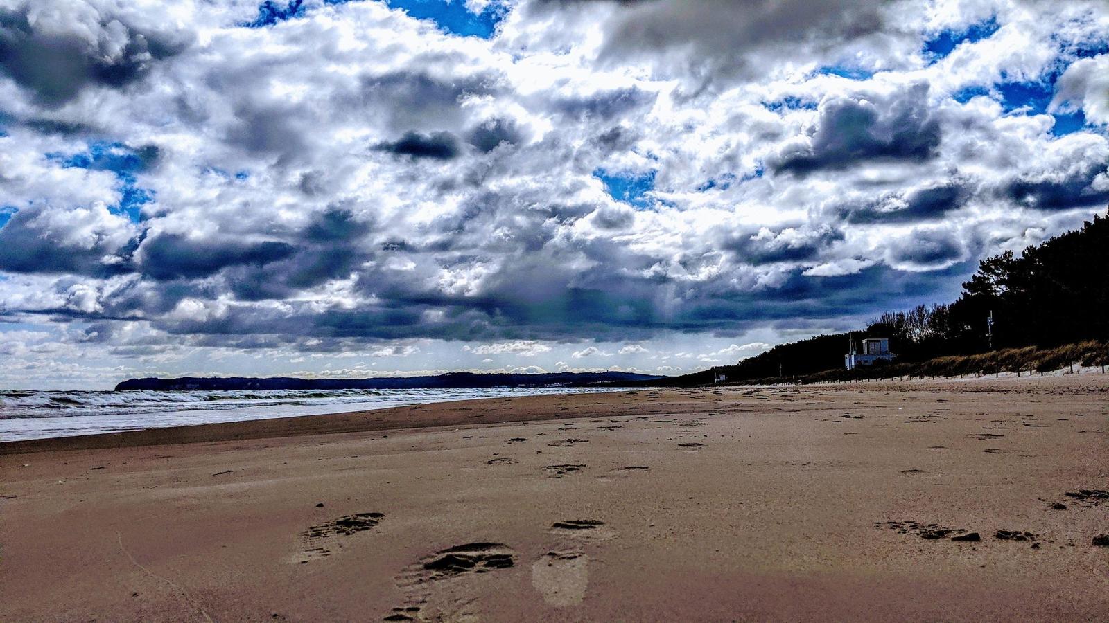Strand mit Fußabdrücken, bewölkter Himmel und Horizont mit Wasser.
