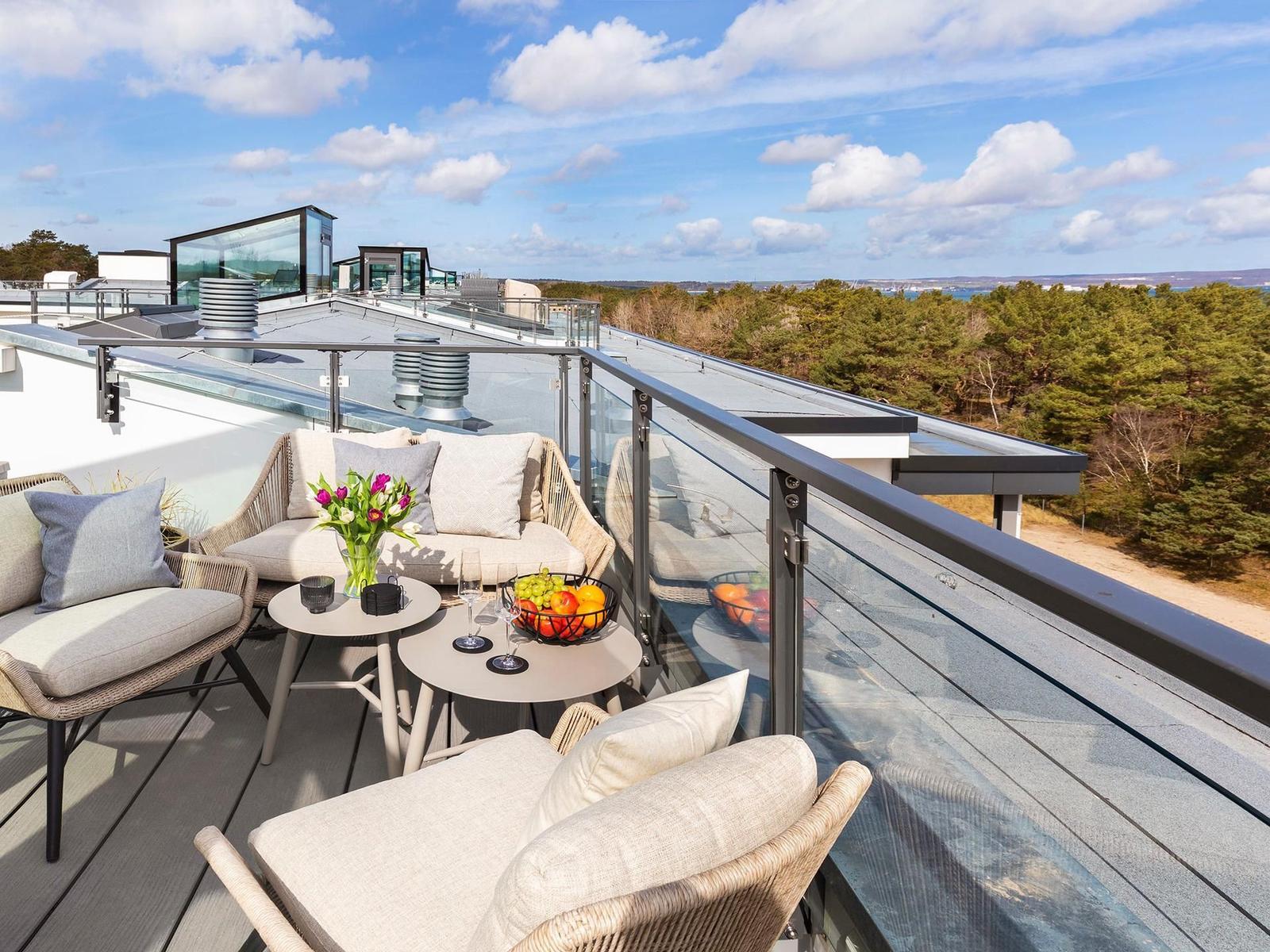 Terrasse mit Sitzgruppe, Tisch und Obst. Blick auf Wald und Himmel.
