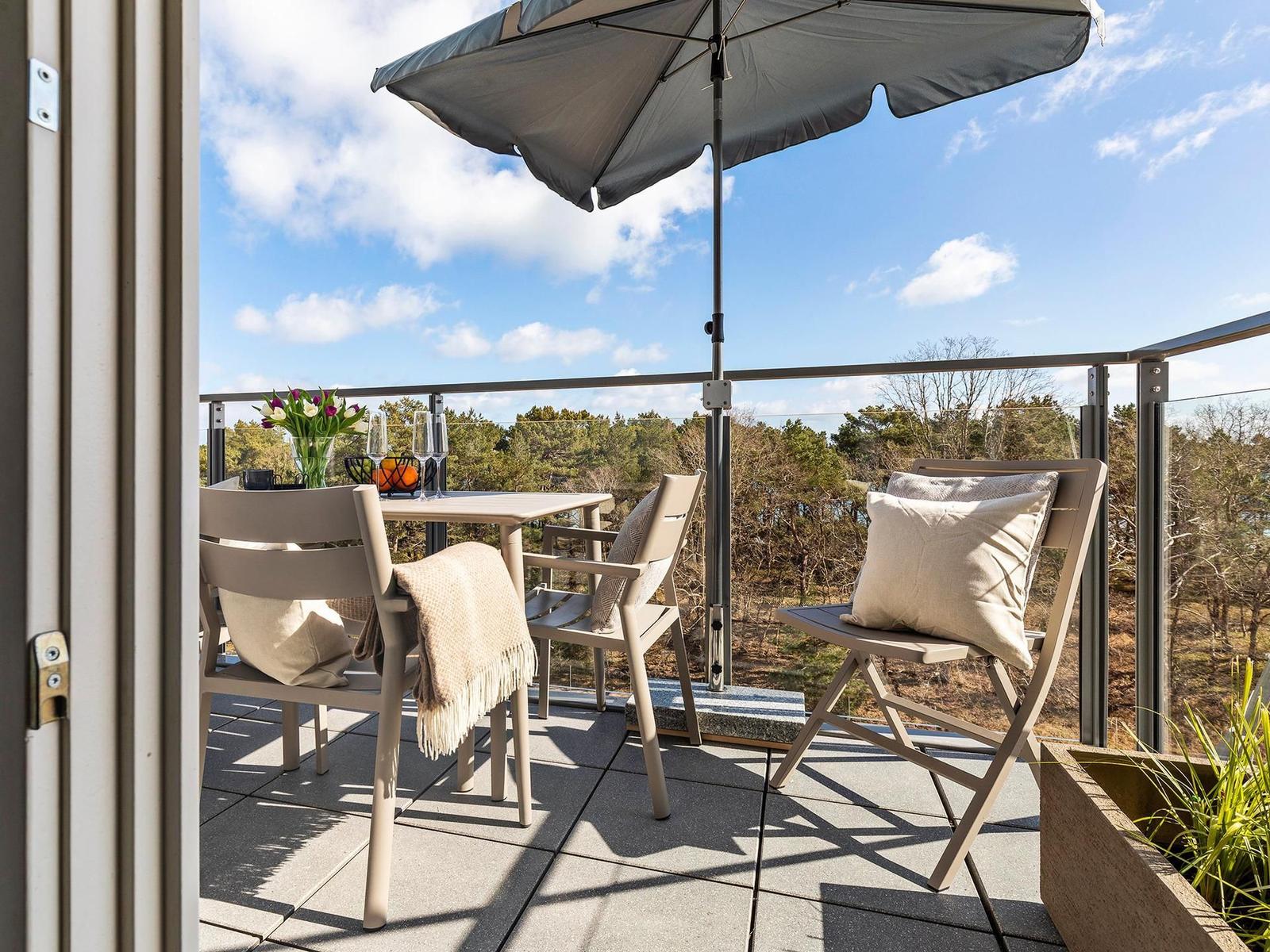 Terrasse mit Tisch, Stühlen und Sonnenschirm. Blick auf Wald und Himmel.