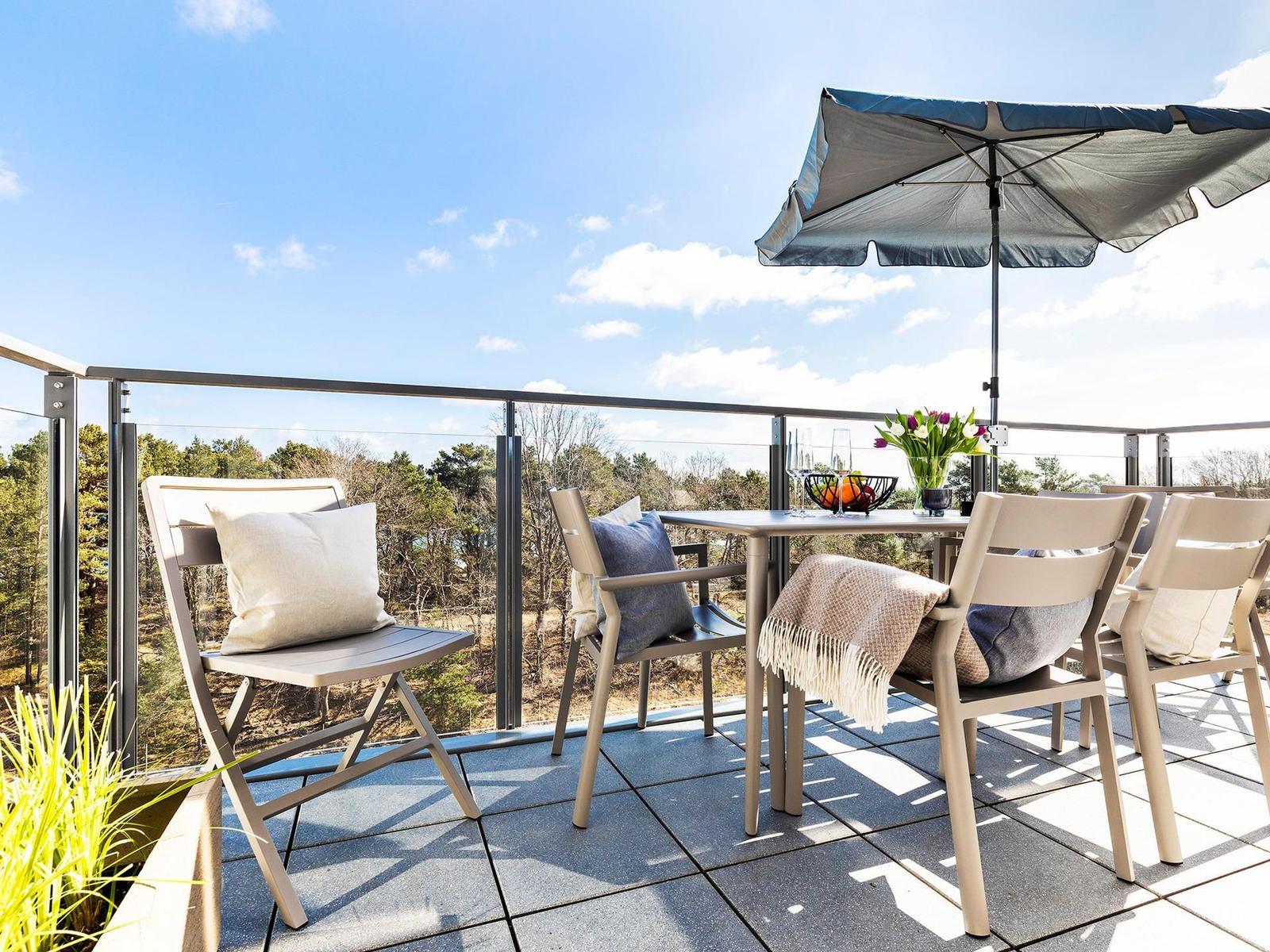 Terrasse mit Tisch, Stühlen und Sonnenschirm. Blick auf Wald und Himmel.