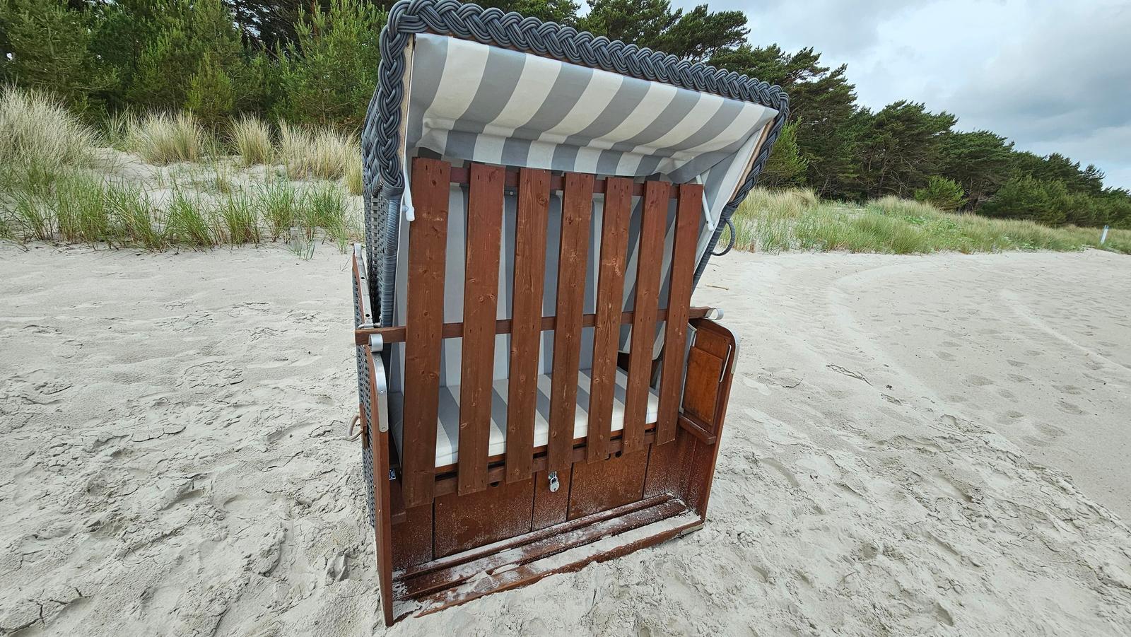 Holzstrandkorb mit gestreifter Plane auf sandigem Strand.