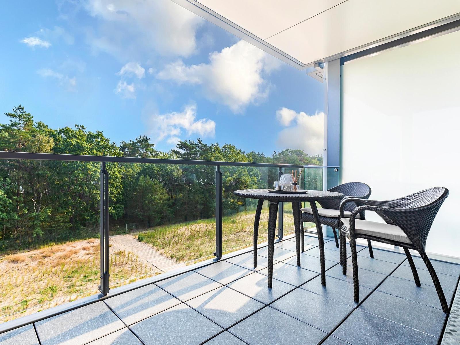 Terrasse mit Tisch und Stühlen, Blick auf Wald und Himmel.