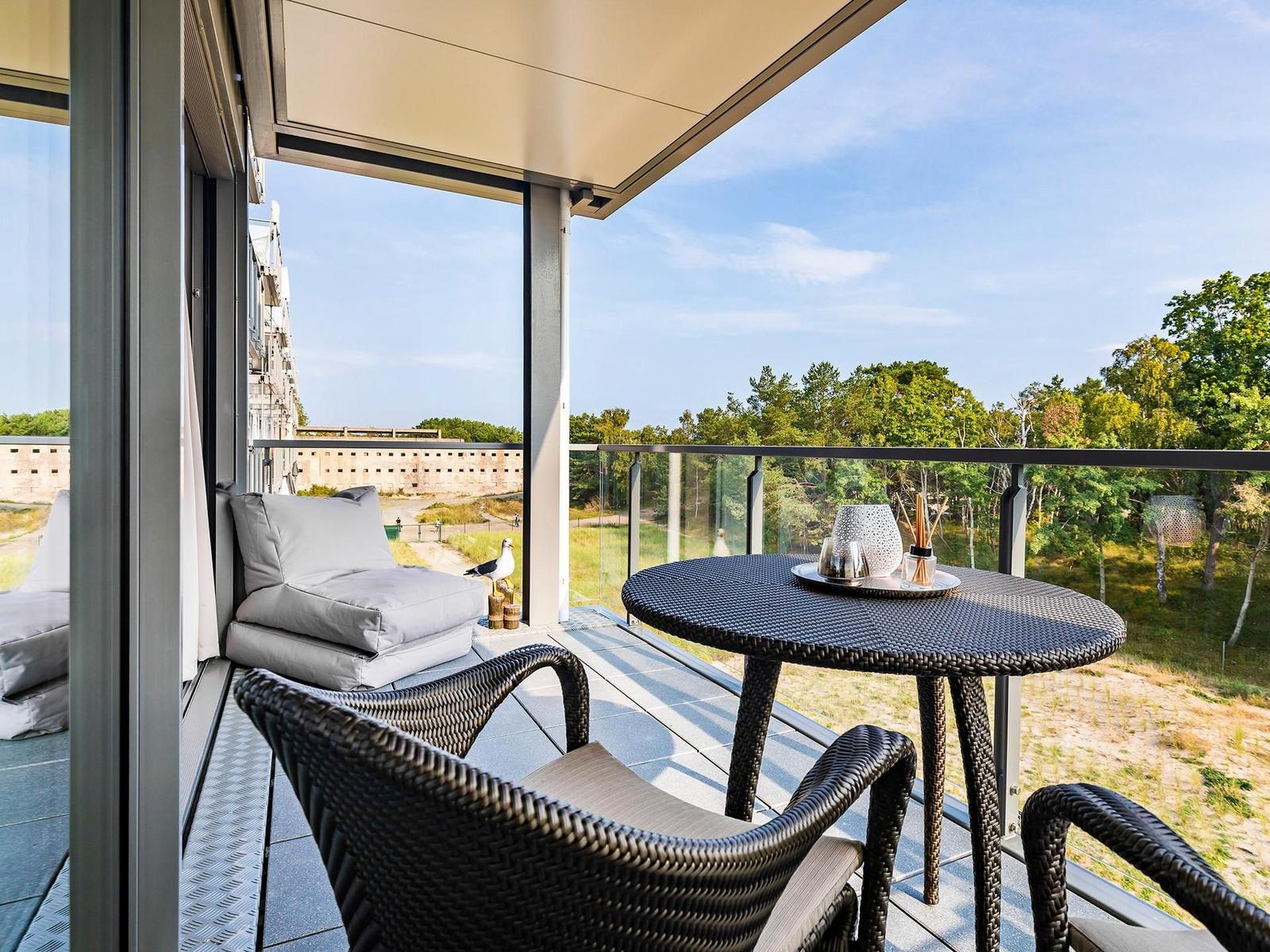 Terrasse mit Sitzgruppe und Tisch. Blick auf Wald und Gebäude.