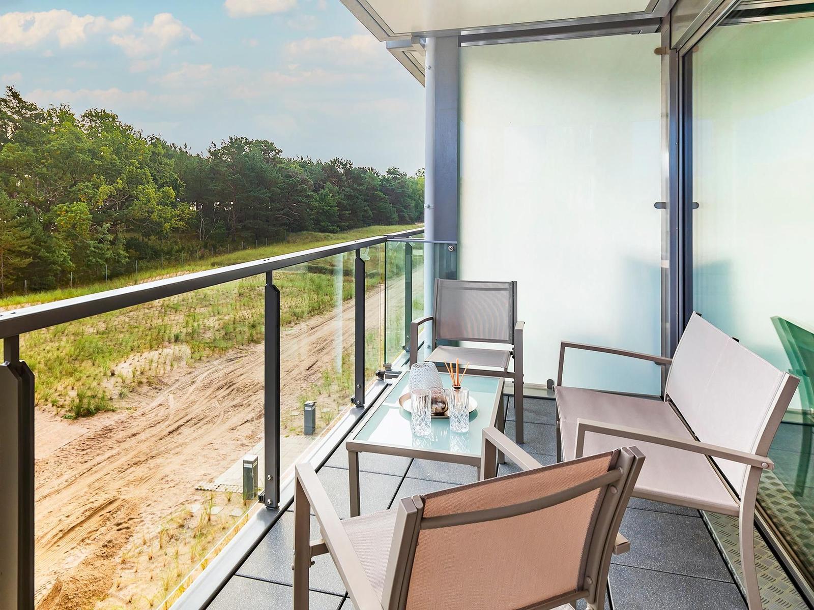 Terrasse mit Sitzgelegenheiten und Blick auf Wald und Strand.