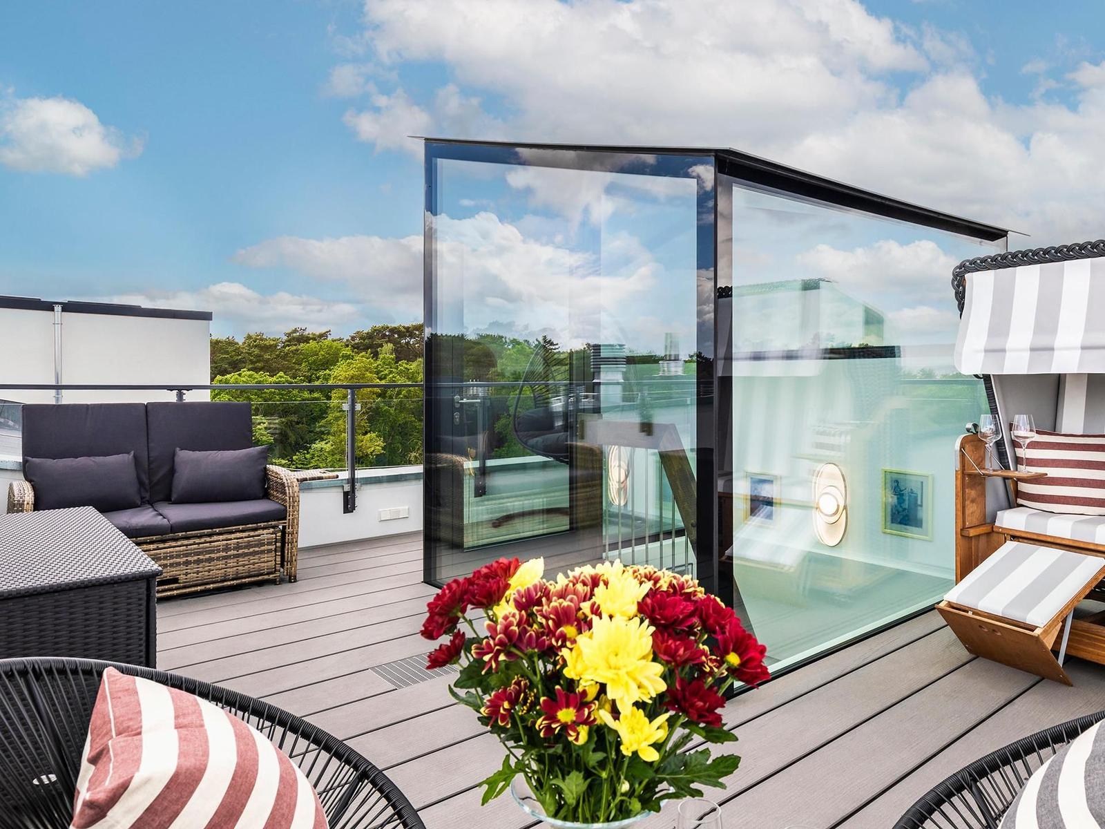 Terrasse mit Glasbau, Sitzgelegenheiten und Blumenarrangement.