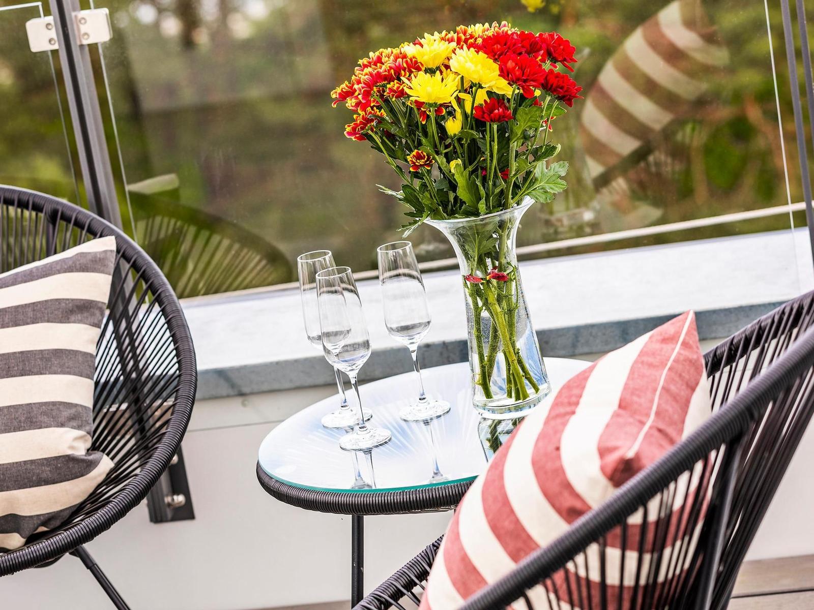 Terrasse mit Tisch, zwei Stühlen und Blumenstrauß in Vase.