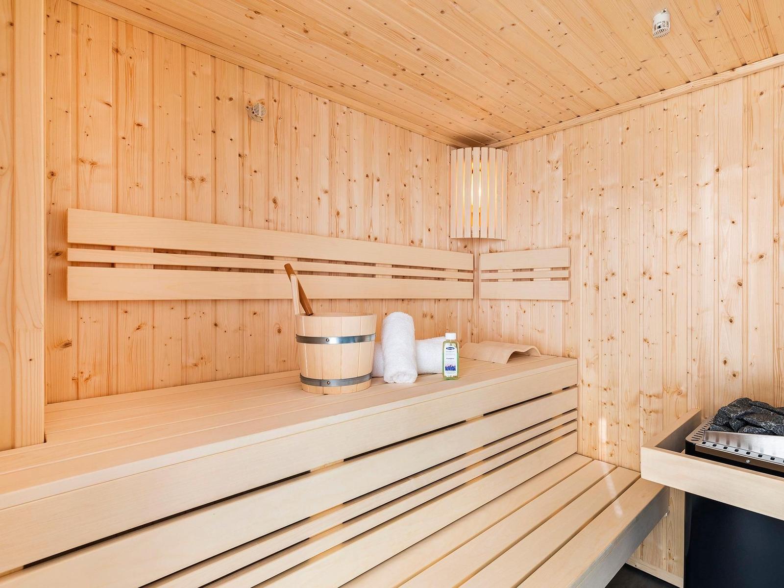 Sauna mit Holzbank, Eimer, Handtuch und Keramikofen.