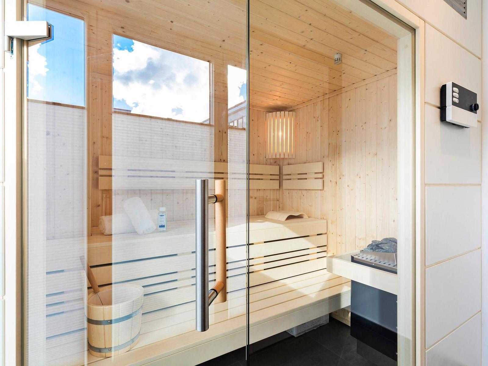Sauna mit Holzbank, Glasfront und Außensicht. Dampfstein und Handtuch bereit.