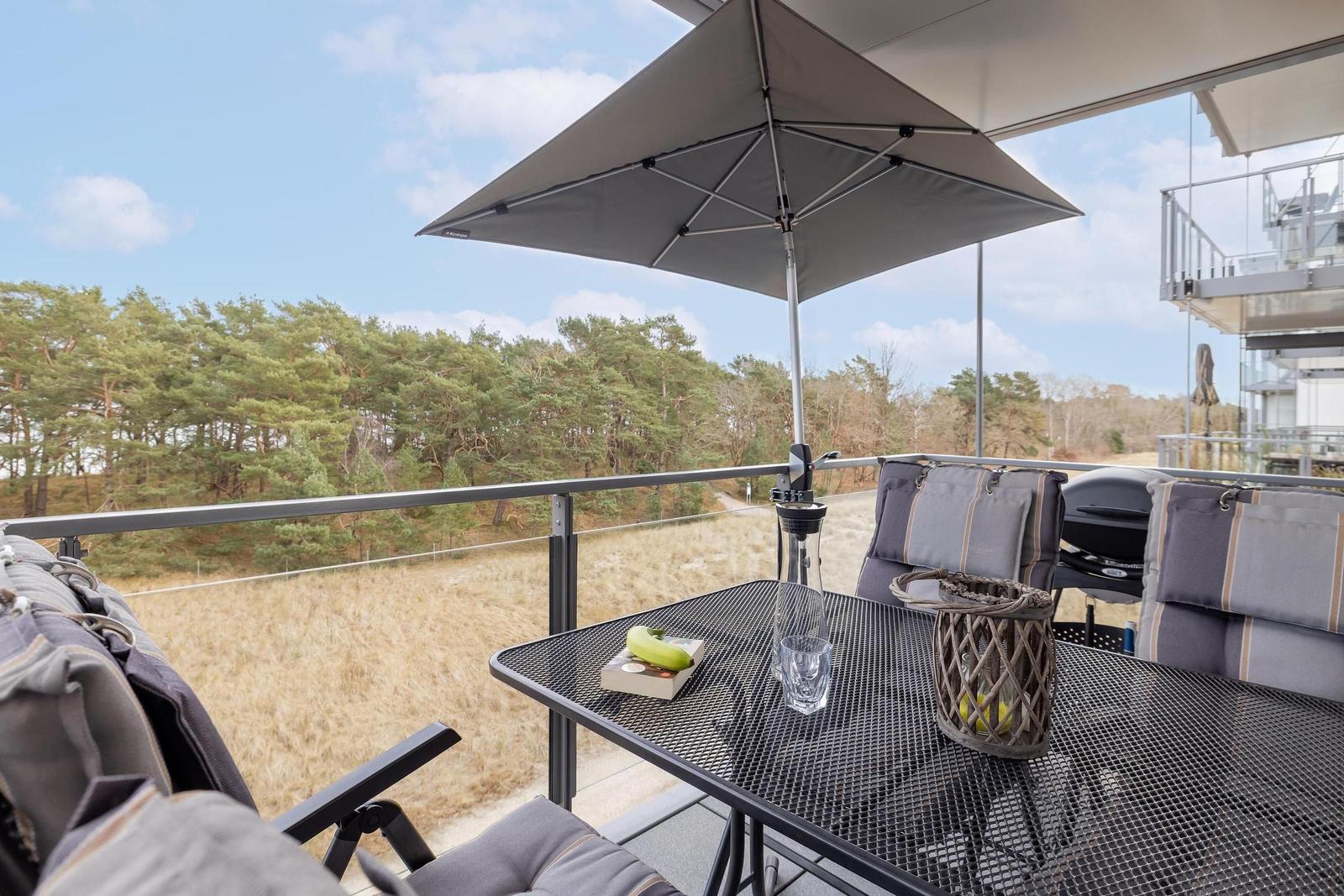 Terrasse mit Tisch, Stühlen und Sonnenschutz. Blick auf Wald und Grasland.