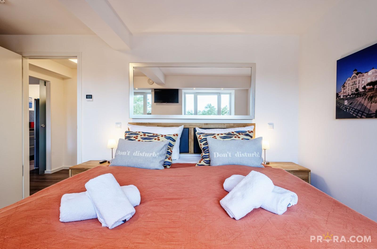 Schlafzimmer mit Doppelbett, Spiegel und Wandbild. Handtuchbündel liegen auf dem Bett.