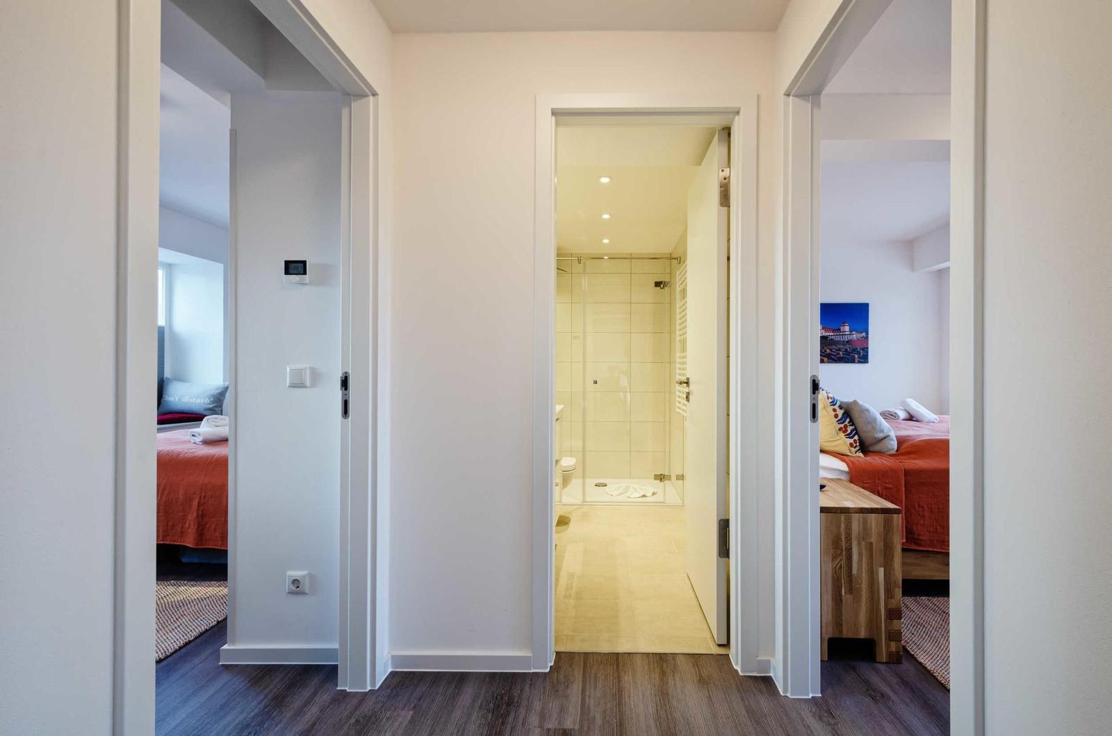 Durchgang mit Blick auf Bad und zwei Schlafzimmer mit Betten und Holzmöbeln.