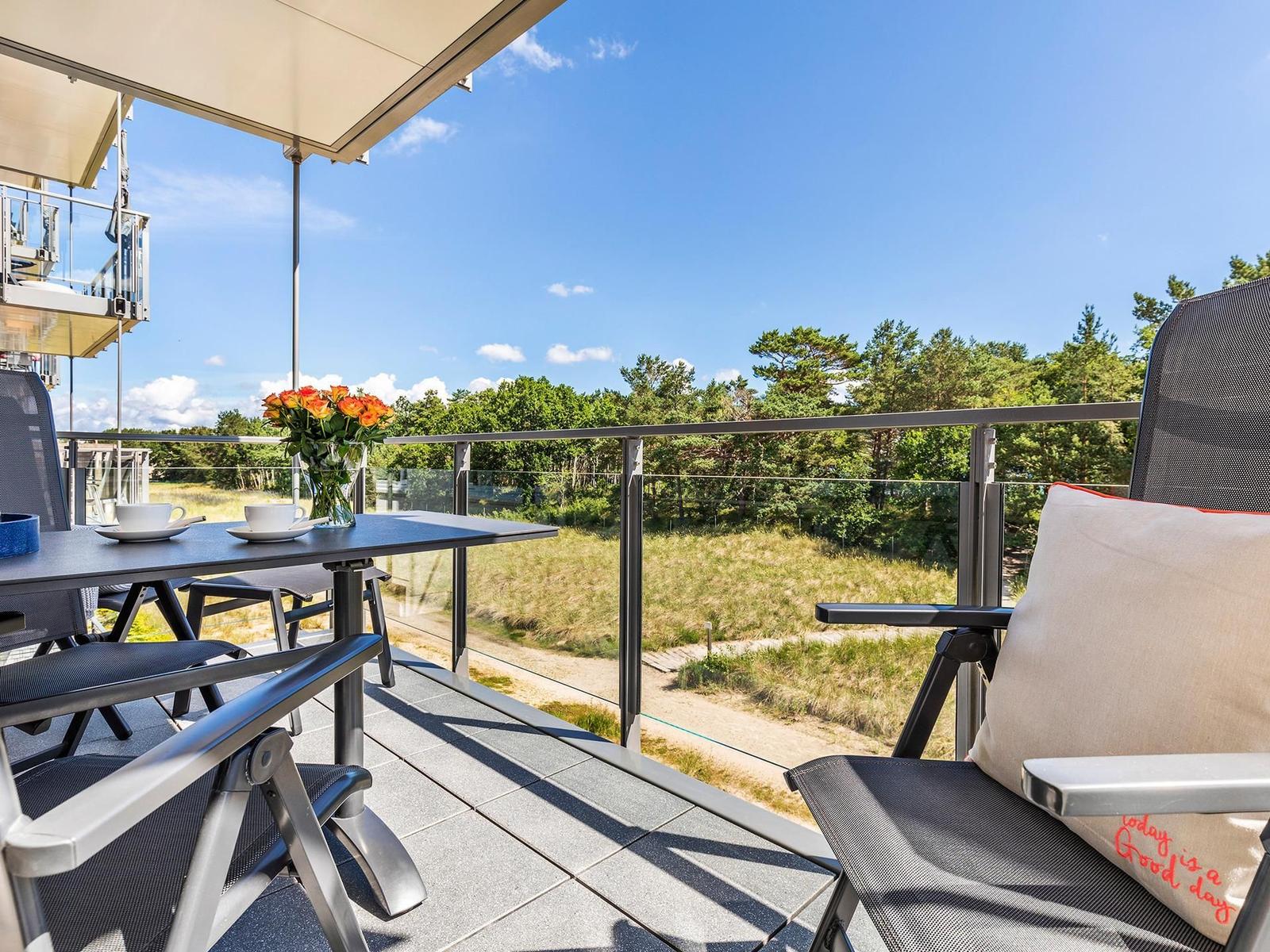 Terrasse mit Tisch, Stühlen und Blick auf Wald und Himmel.