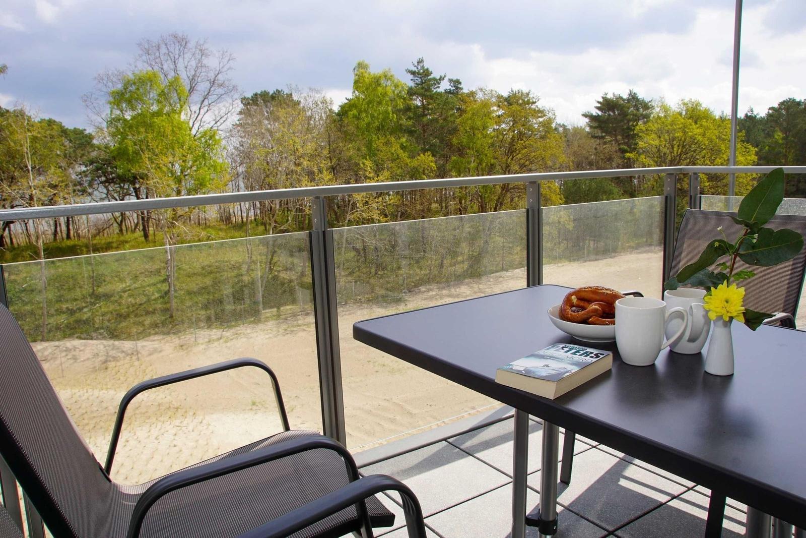 Terrasse mit Tisch, Stühlen und Blick auf Wald und Sanddünen.