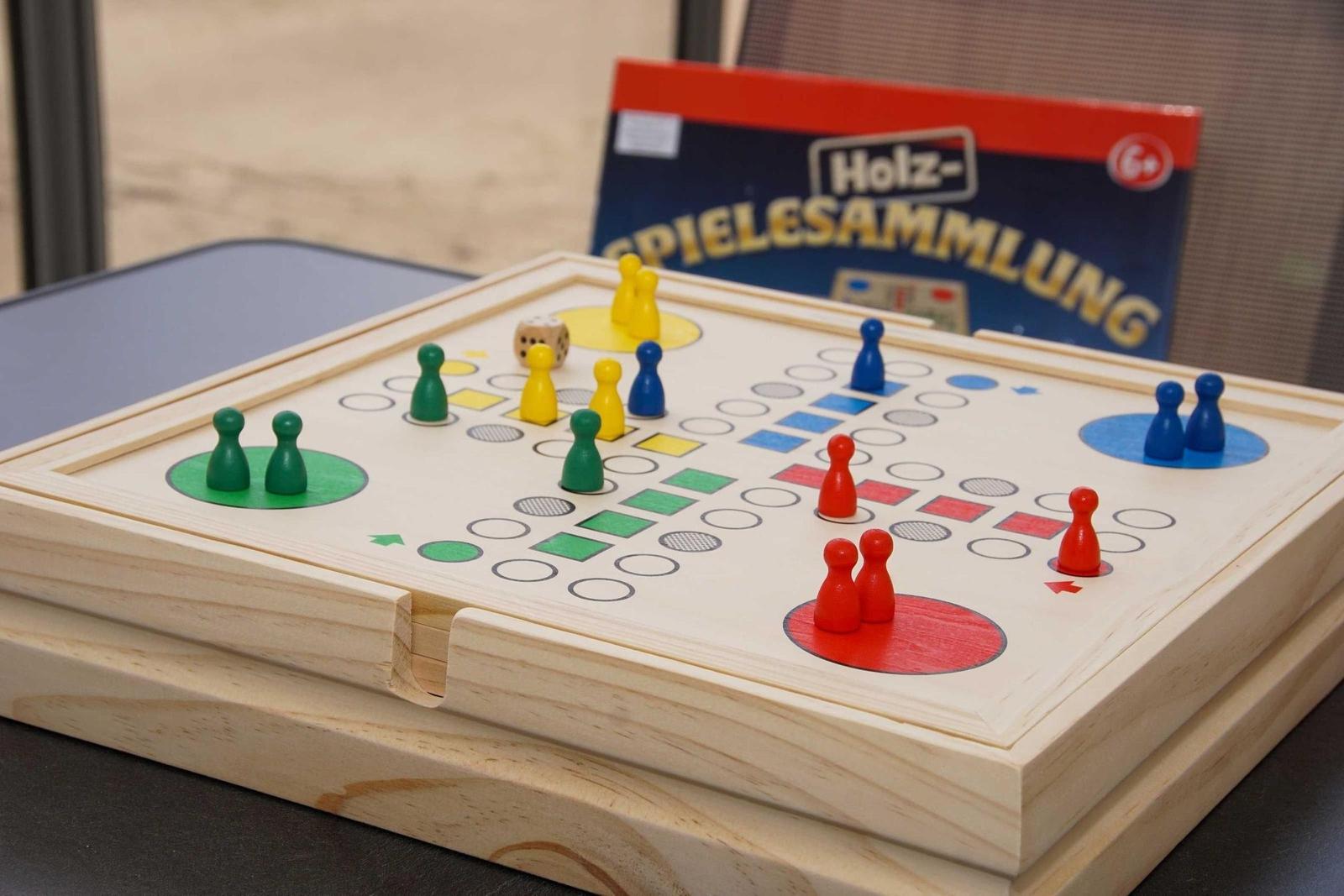 Holzspielbrett mit bunten Spielsteinen und Würfel. Hintergrund: Spielbox mit Aufschrift.