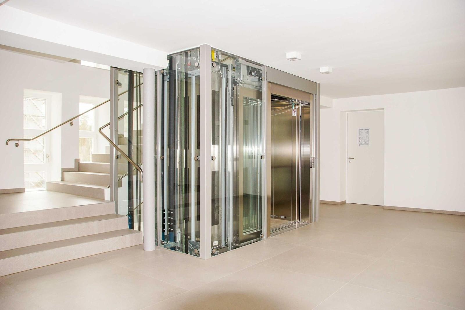 Modernes Liftsystem mit Glasfassade neben Treppe im Eingangsbereich.