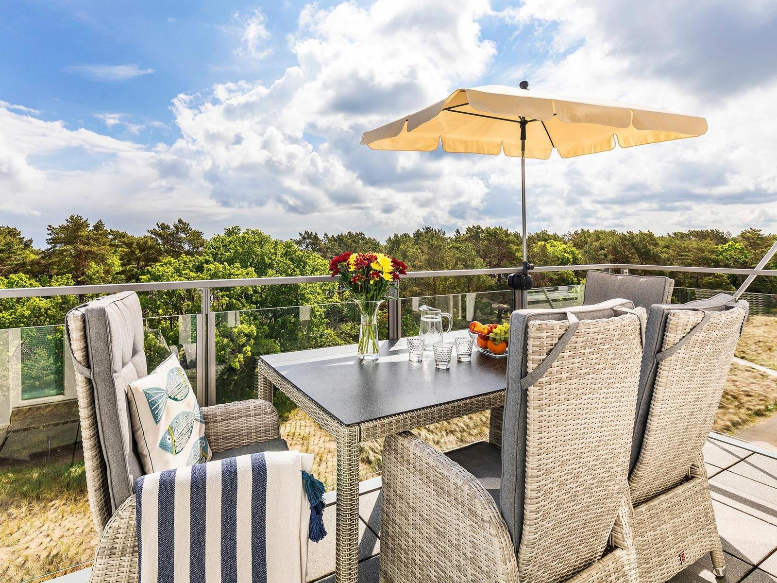 Terrasse mit Tisch, Stühlen und Sonnenschirm. Blick auf Wald und Himmel.