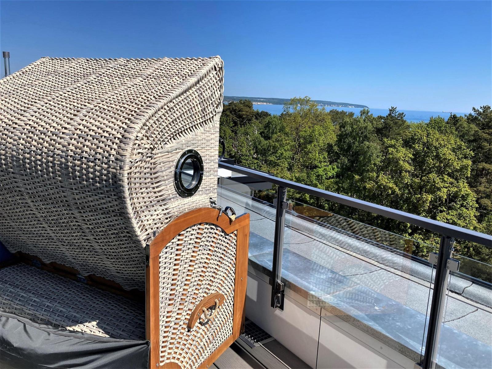 Terrasse mit Rattanliege und Blick auf Wald und Meer.