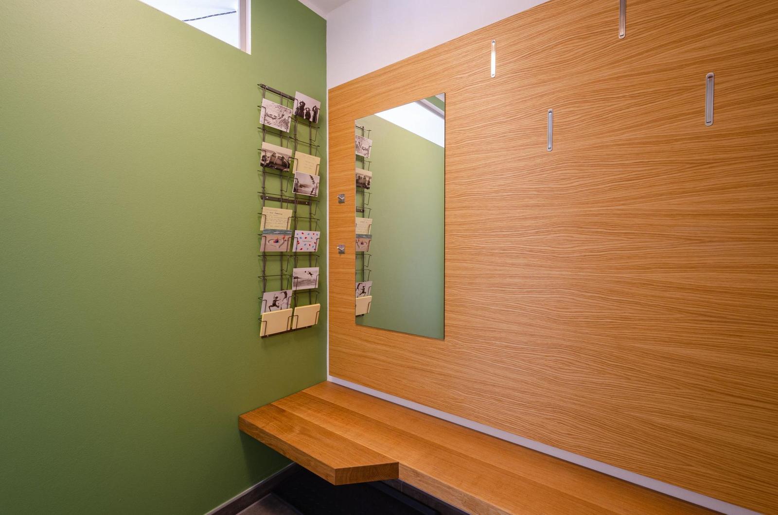 Helle Ecke mit grüner Wand, Holzbank und Spiegeltür. Kartenhalter an der Wand.