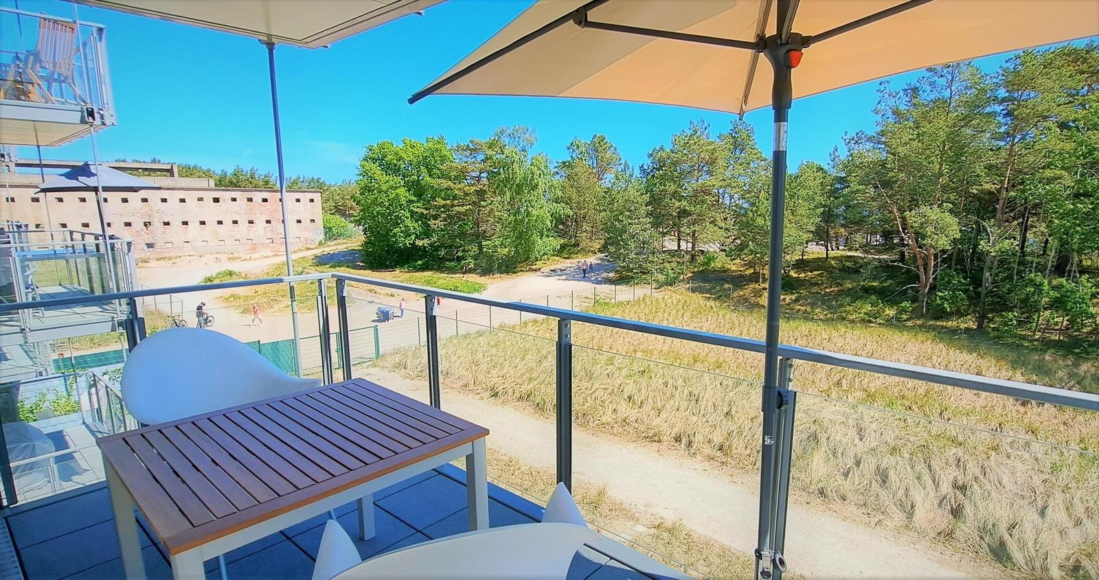 Terrasse mit Tisch, Stühlen und Sonnenschirm. Blick auf Wald und Gebäude.