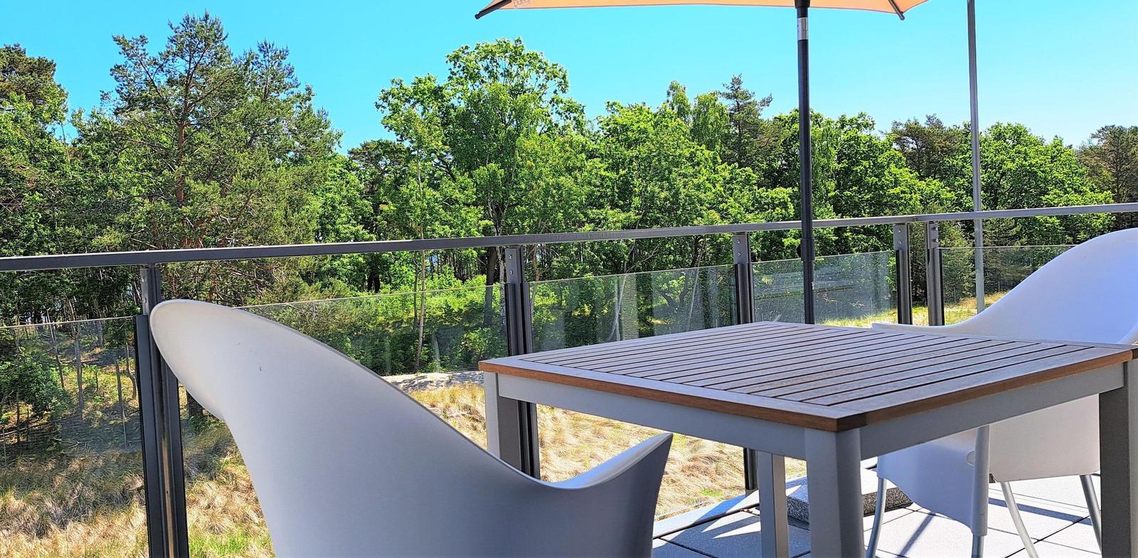 Terrasse mit Tisch, Stühlen und Sonnenschirm. Blick auf grüne Bäume und Himmel.