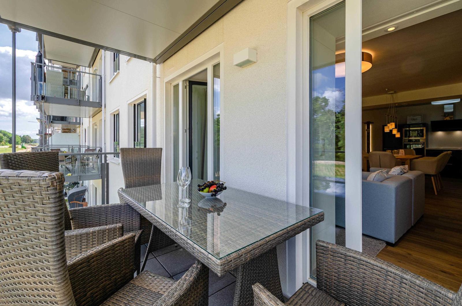 Terrasse mit Glas-Tisch und Stühlen. Durchgehendes Glas führt ins Wohnzimmer.