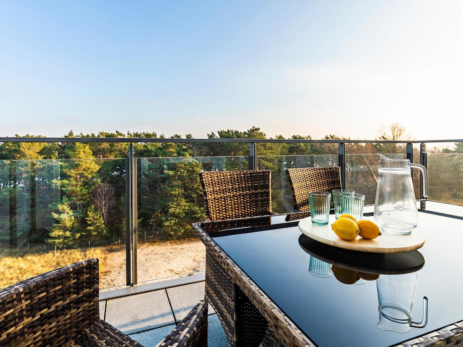 Terrace with glass railing, table, chairs, and fruit. View of forest.