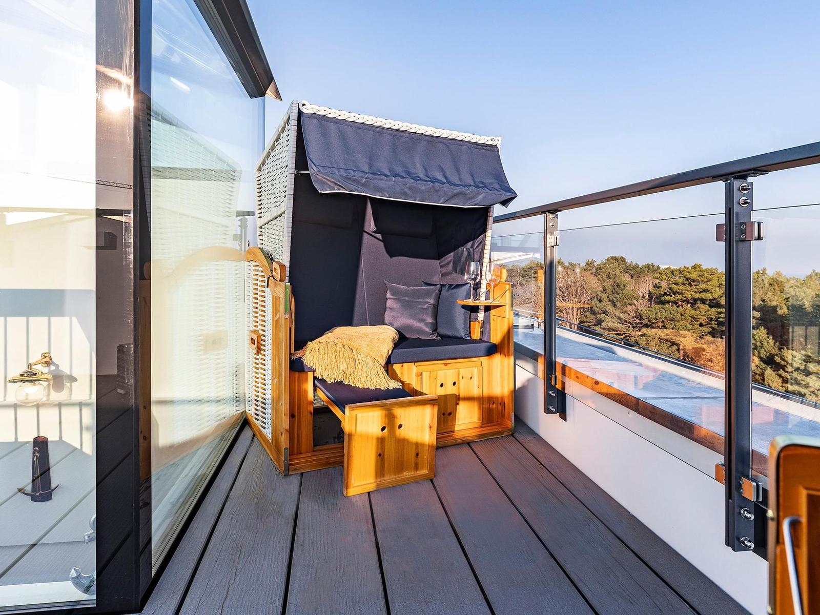 Terrace with wooden lounger, dark blue canopy, and view of forest.