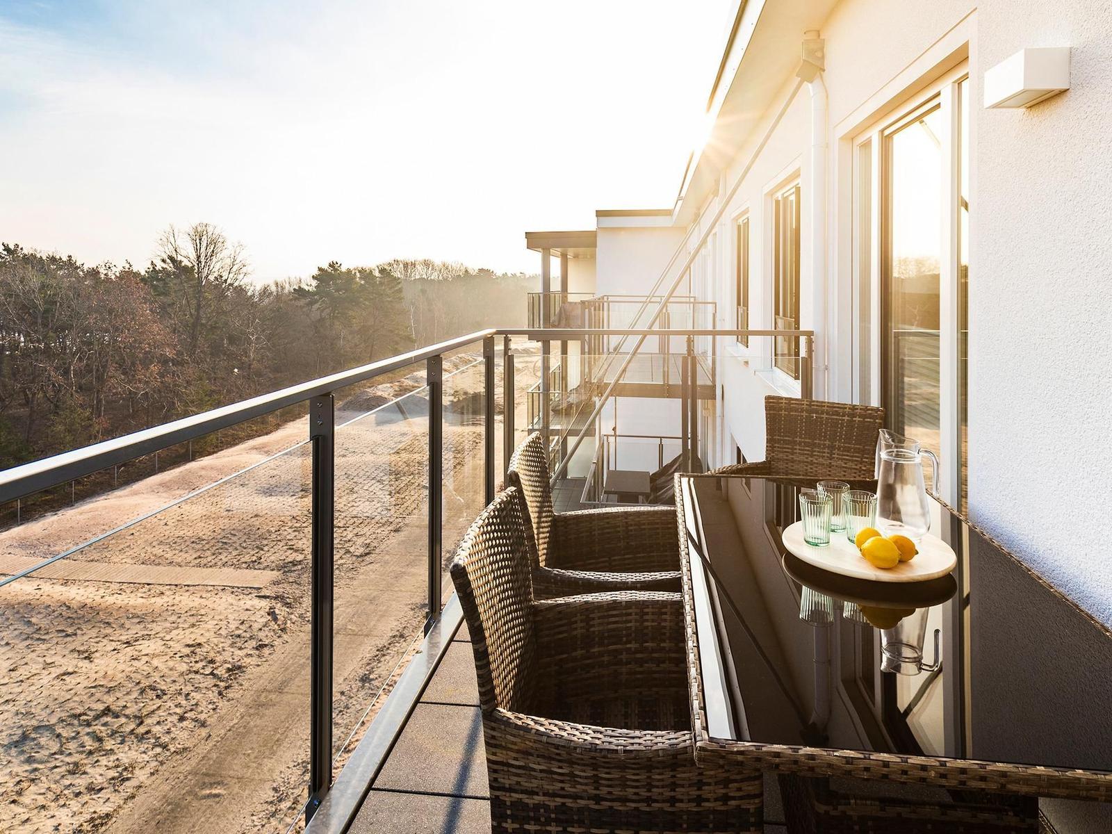 Terrace with table and chairs, view of forest and sandy beach.