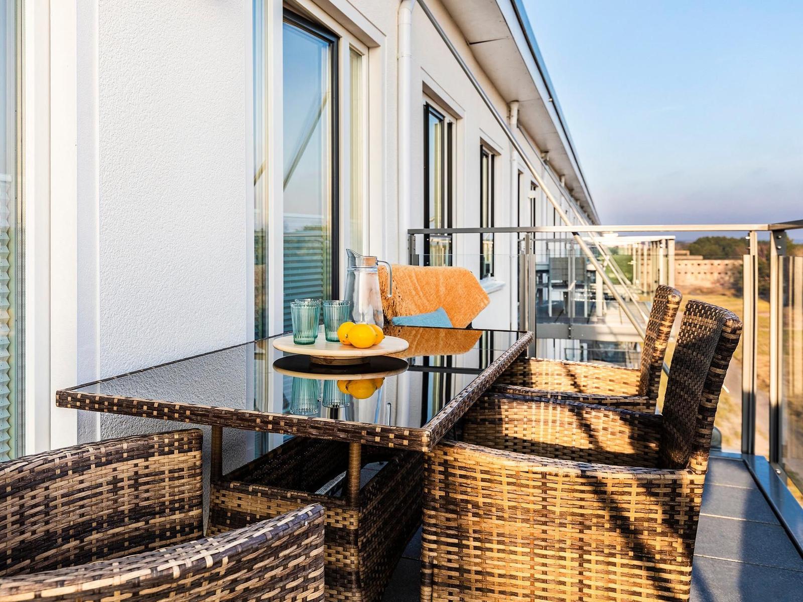 Terrace with table, chairs, and drinks. View of buildings and landscape.