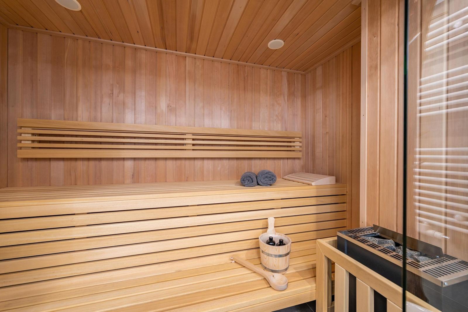 Sauna mit Holzbank, Handtuch und Eimer mit Flaschen.
